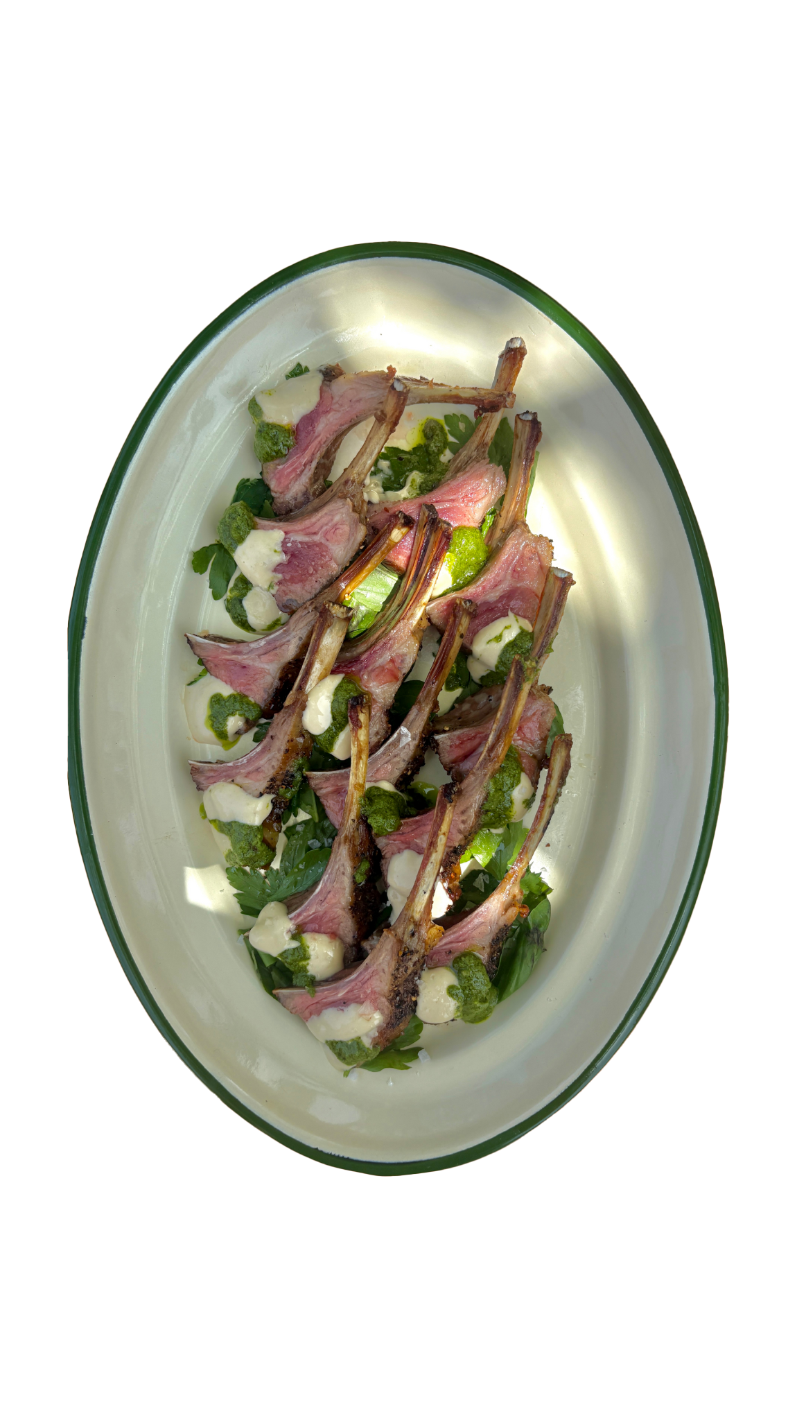 Elegant oval plate with lamb chops served on fresh herb salad with diced vegetables and green sauce.