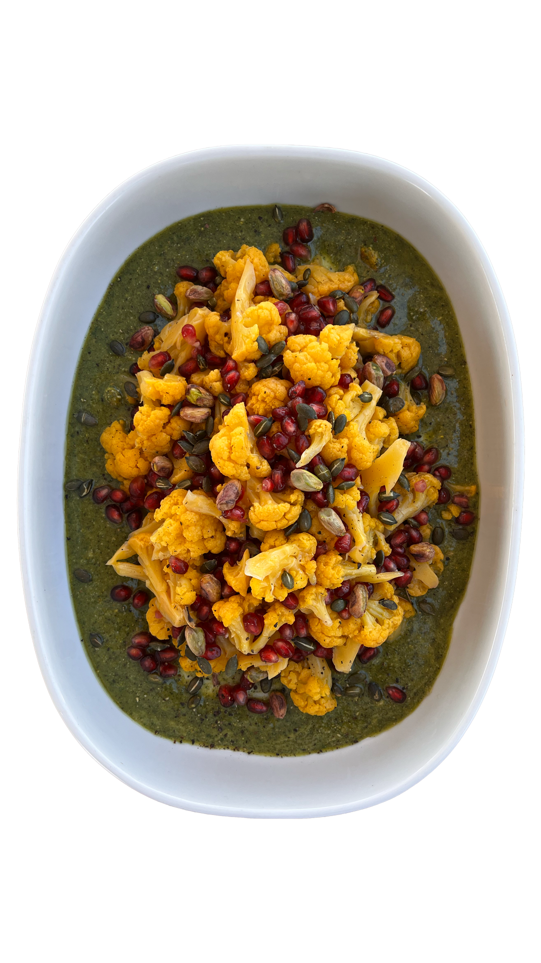 Roasted turmeric cauliflower with pomegranate seeds and pumpkin seeds on green herb sauce in white dish.