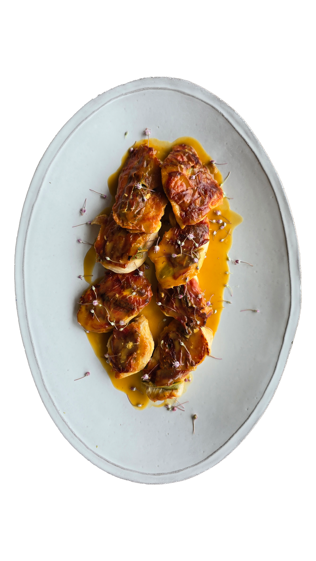 Caramelized rolled cabbage parcels in vibrant orange saffron sauce garnished with microgreens on a rustic gray oval plate.
