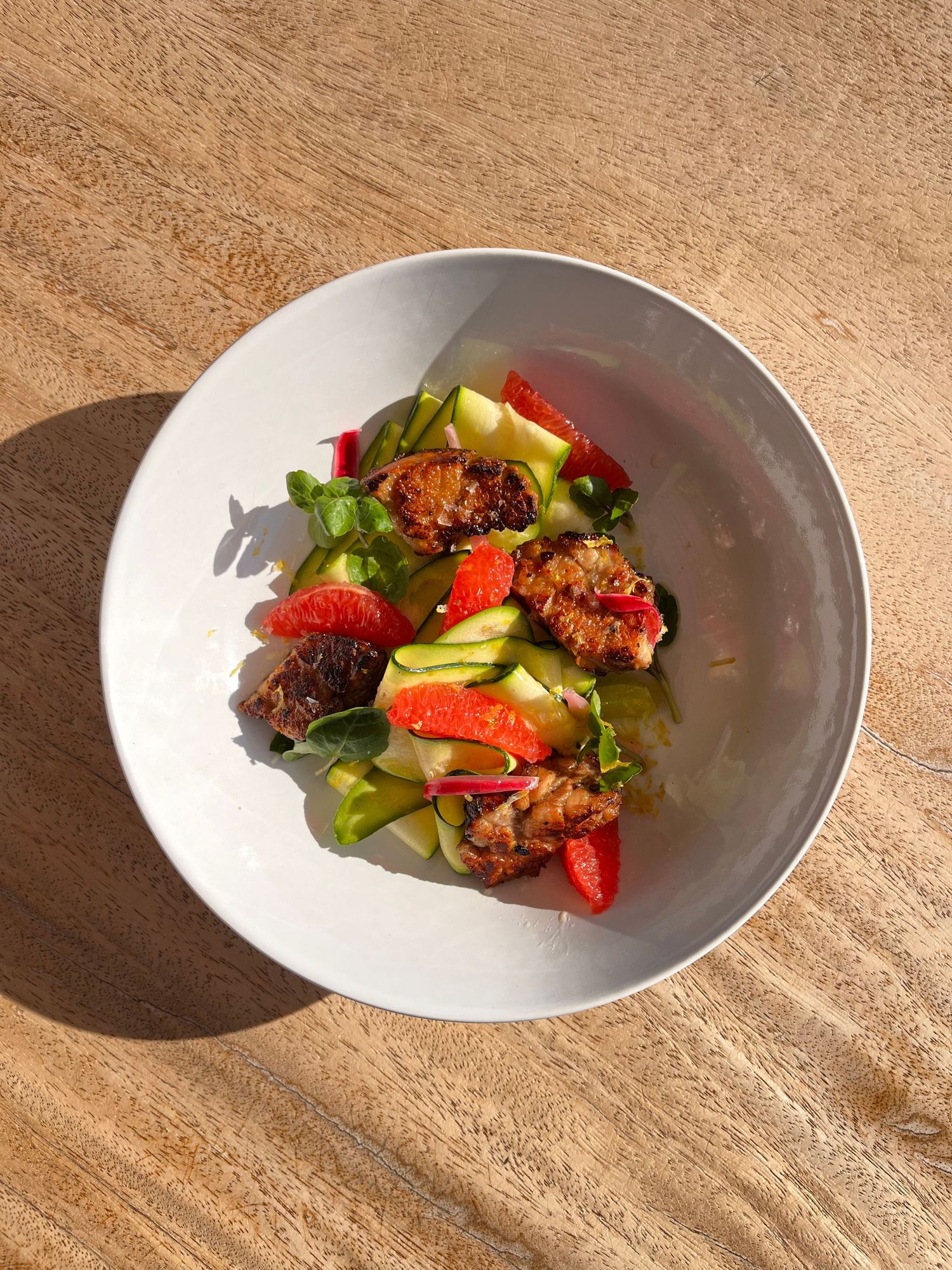 Fresh salad bowl with grilled chicken, strawberries, cucumber, and greens in a white bowl.