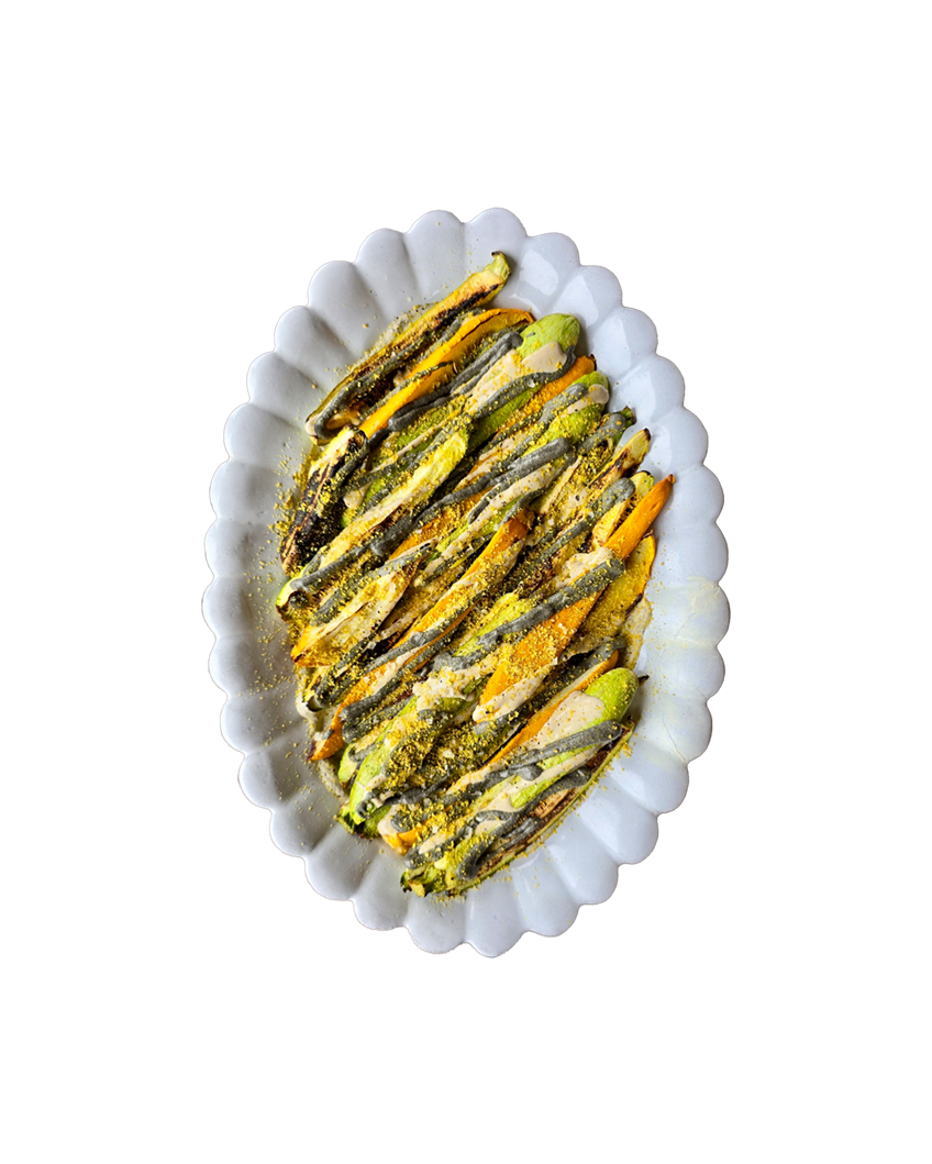 Oven-roasted anchovies coated in turmeric and green herb sauce arranged on a white scalloped decorative oval platter.
