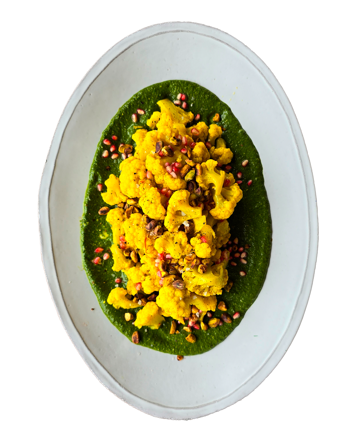 Turmeric roasted cauliflower on green herb sauce topped with pomegranate seeds and pistachios on oval plate.