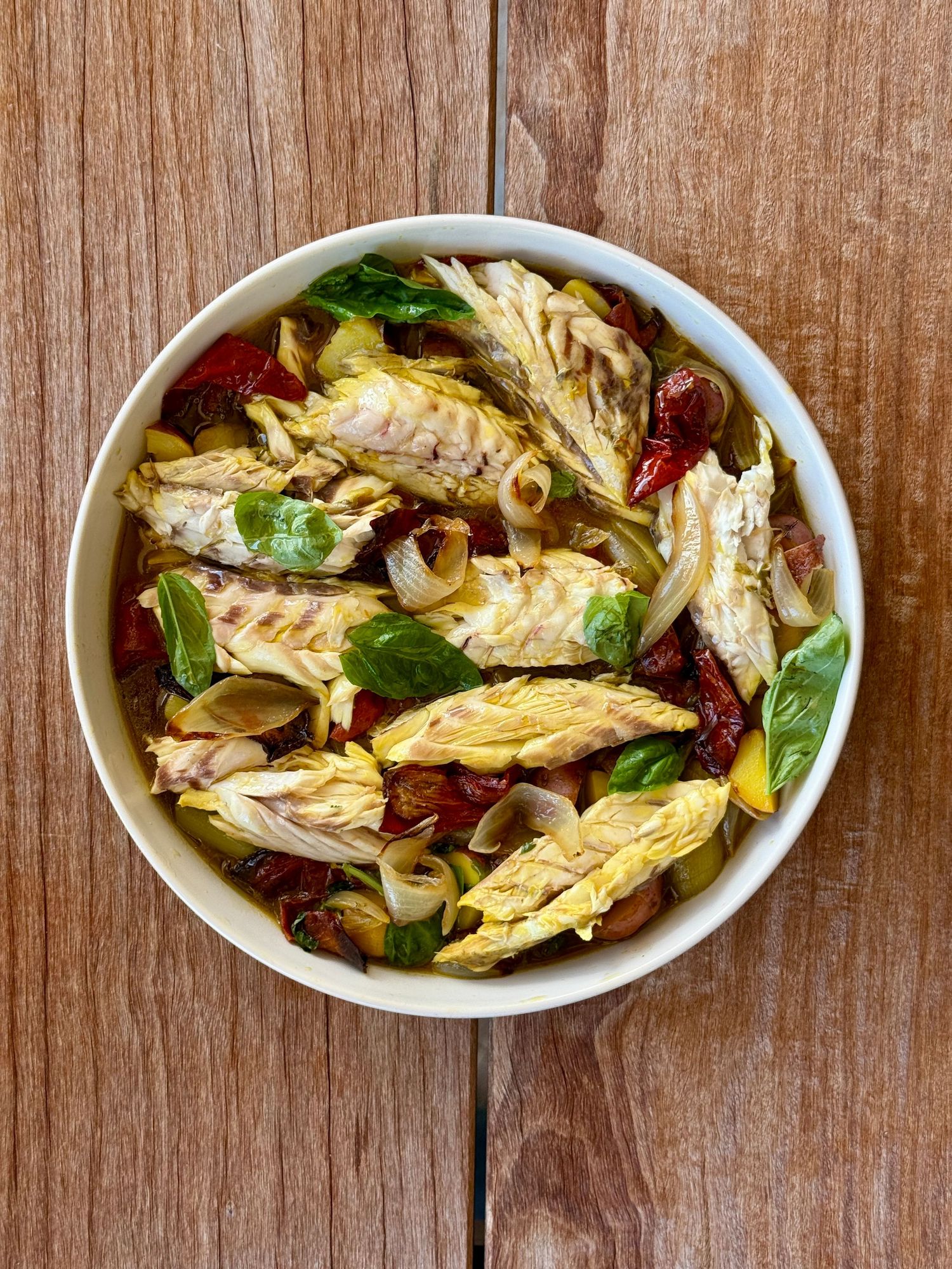 Braised cabbage salad with sun-dried tomatoes, clams, and fresh basil in a white bowl.