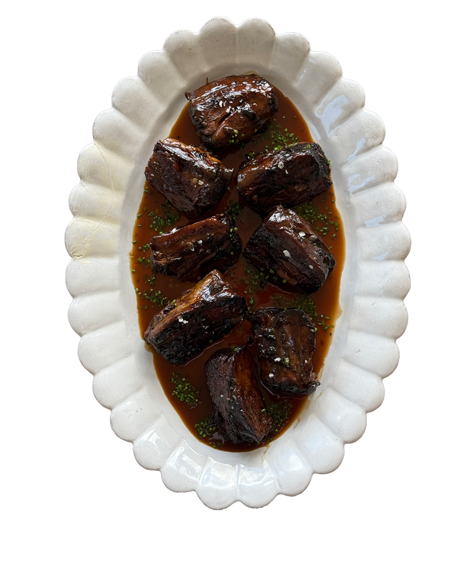Braised beef short ribs in rich brown gravy served on a white scalloped oval platter, garnished with fresh herbs.