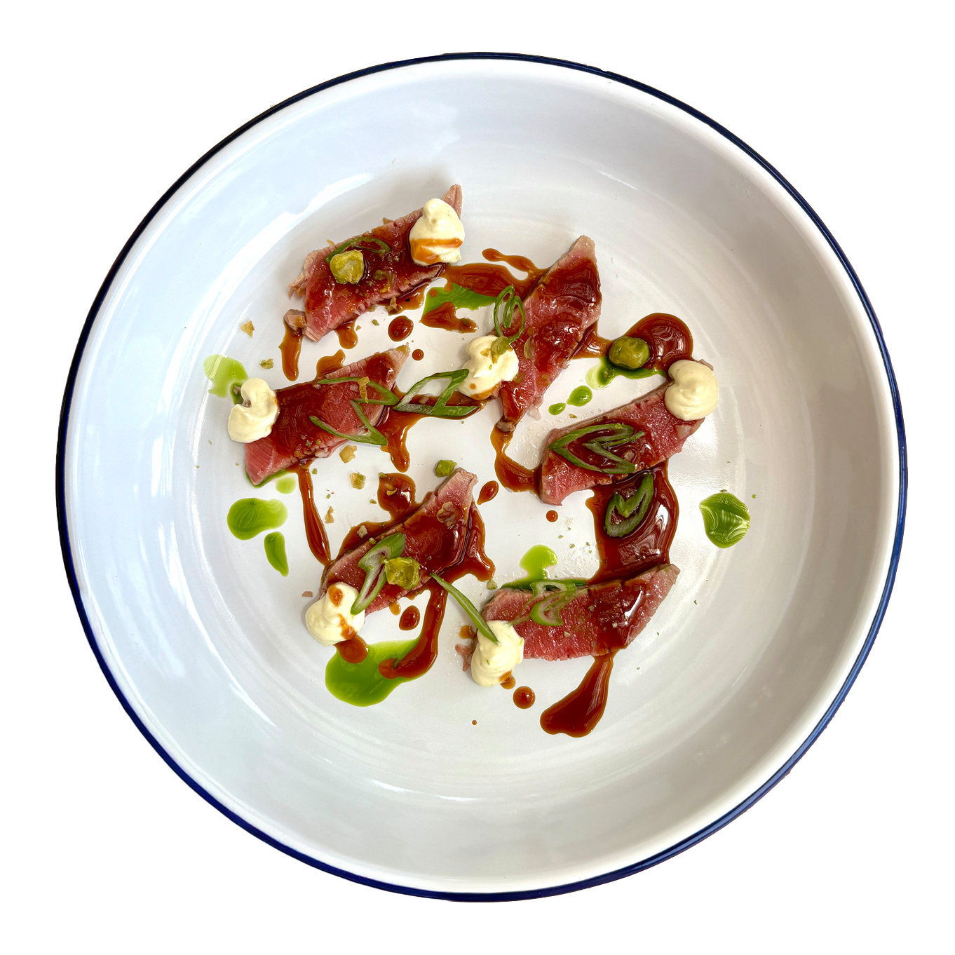 Elegant beef carpaccio dish with green herb sauce, cream, and dark glaze served in a white bowl with blue rim.