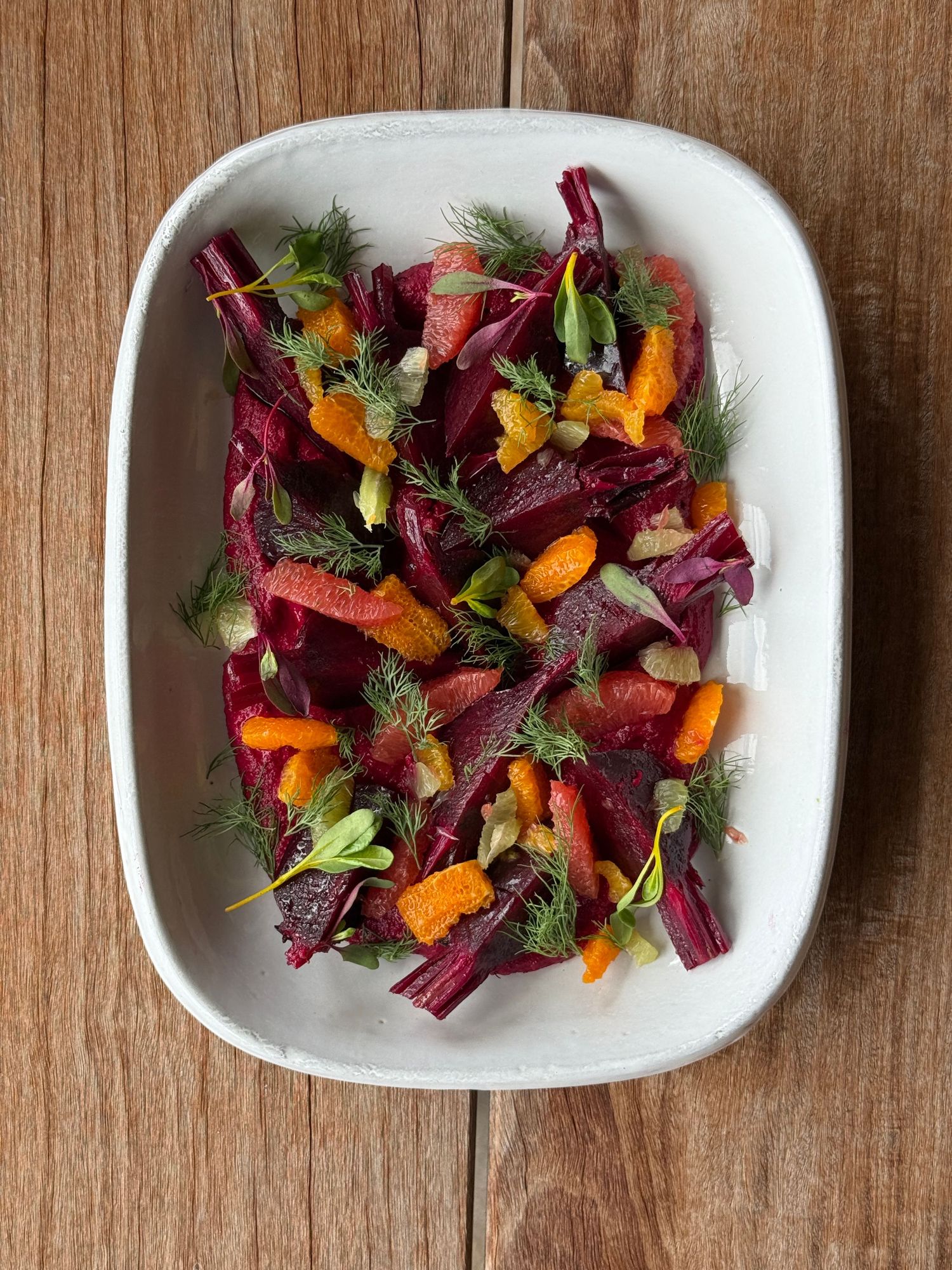 Roasted beet and carrot salad with dill and citrus segments in a white rectangular dish.