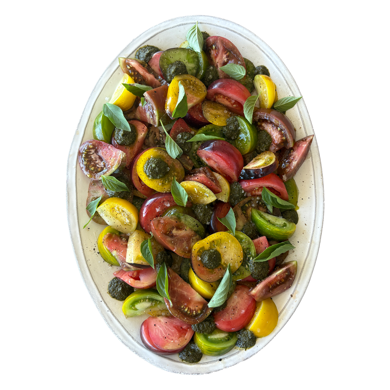Colorful heirloom tomato salad with fresh basil and capers on a white oval platter.