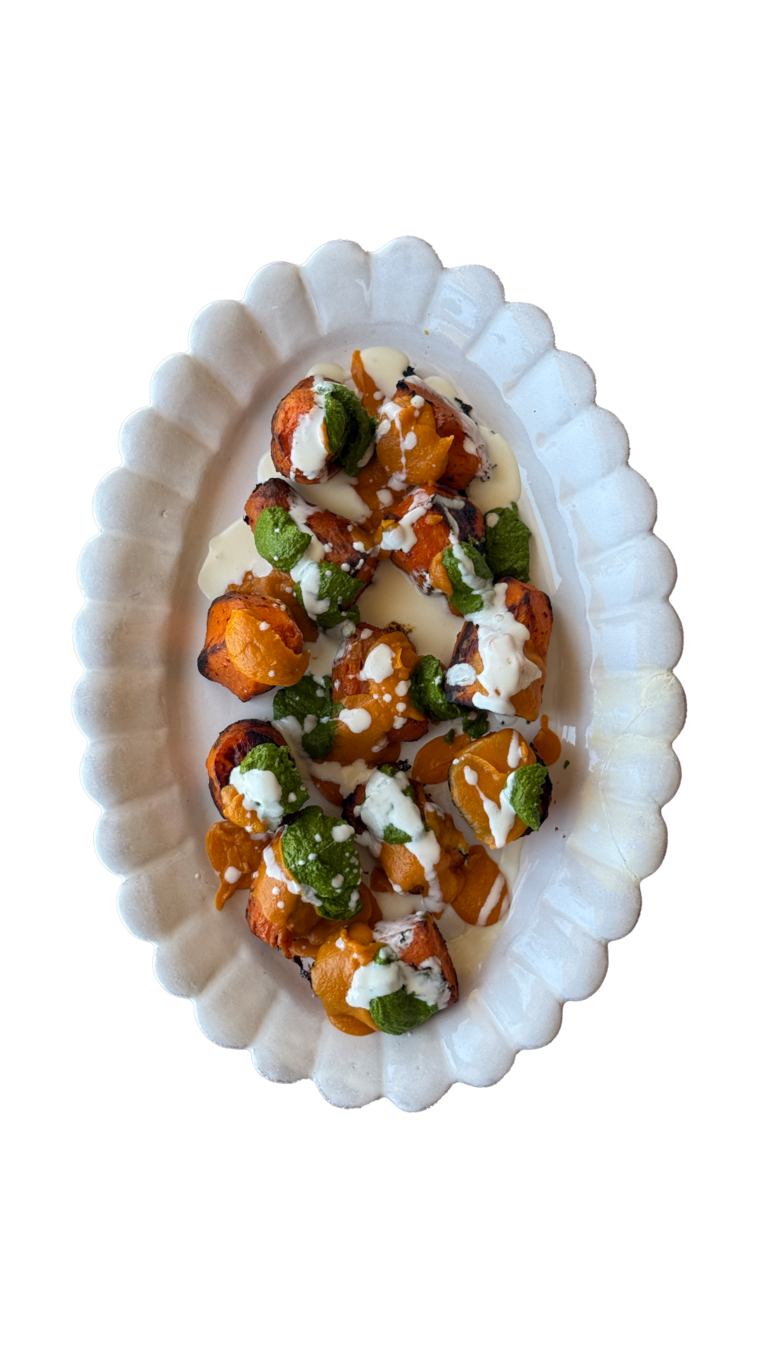 Roasted vegetables with white cream drizzle and fresh herbs served on an elegant oval white scalloped platter.