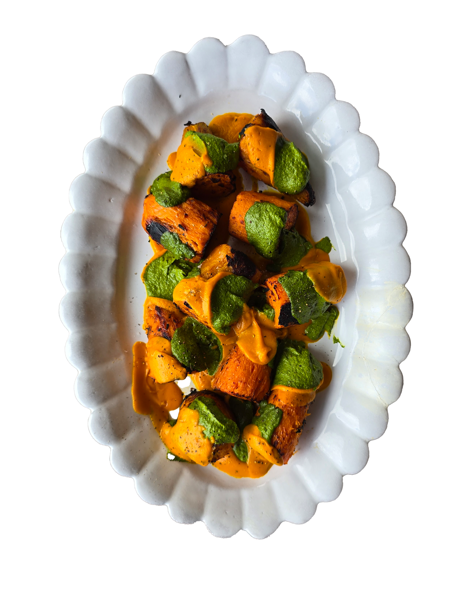 Roasted sweet potato chunks with green herb sauce on white scalloped oval serving platter.