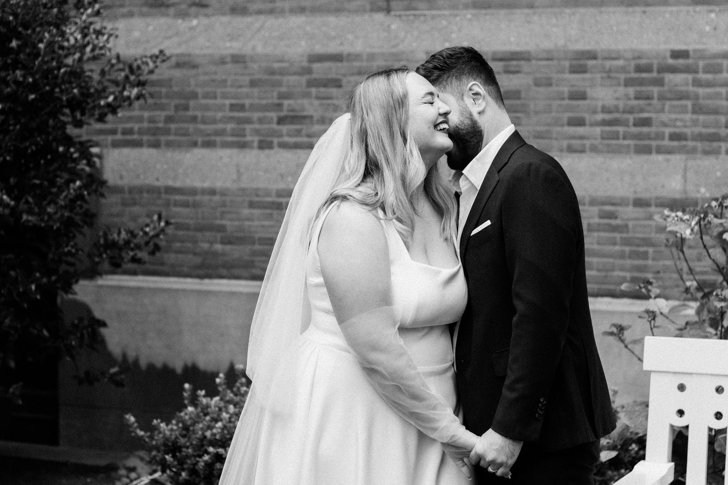 Black and white photo of bride and groom holding hands and smiling at each other outdoors.