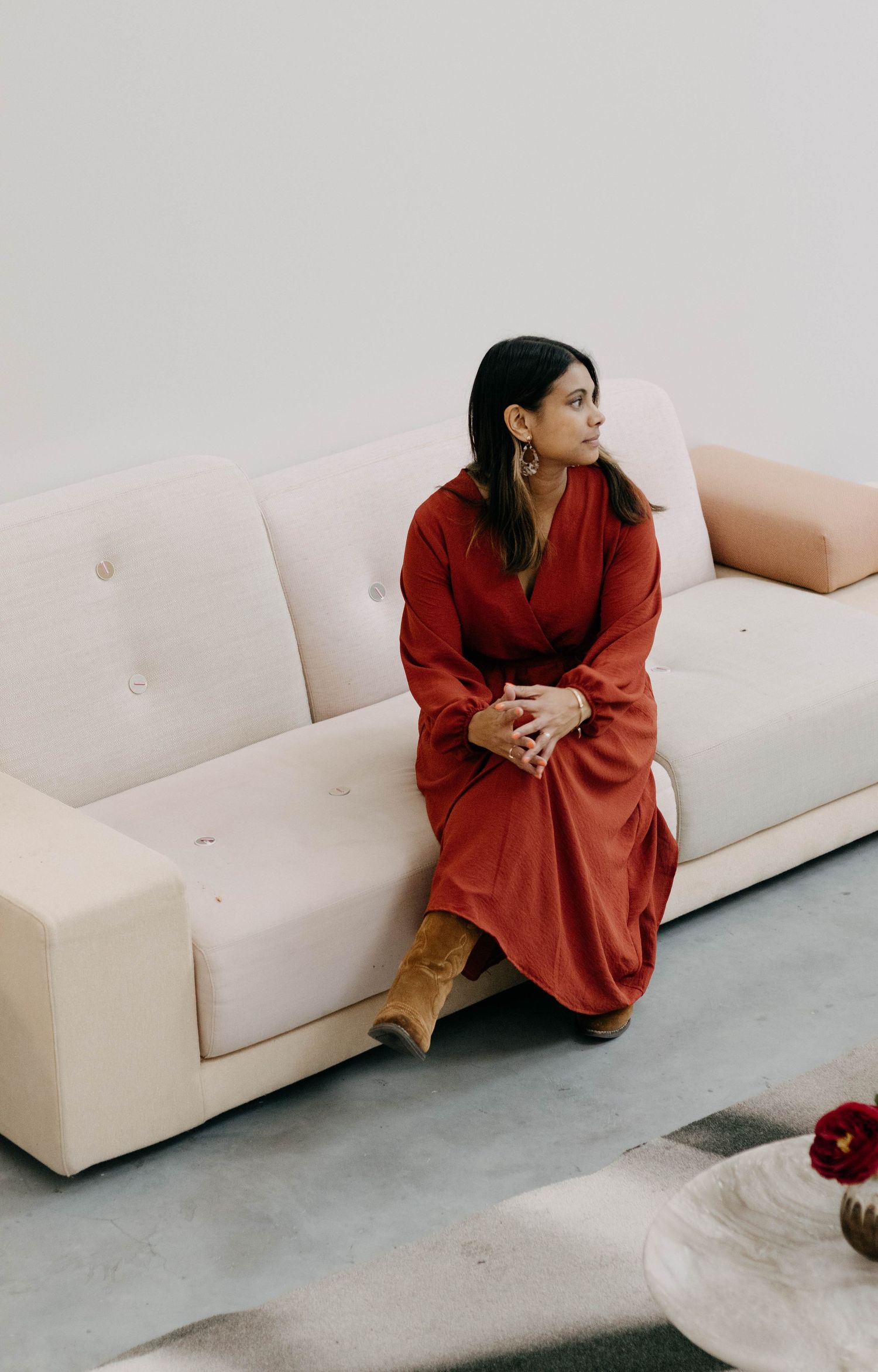 Elegant woman in red wrap dress sitting on a cream sofa in a minimalist modern interior.