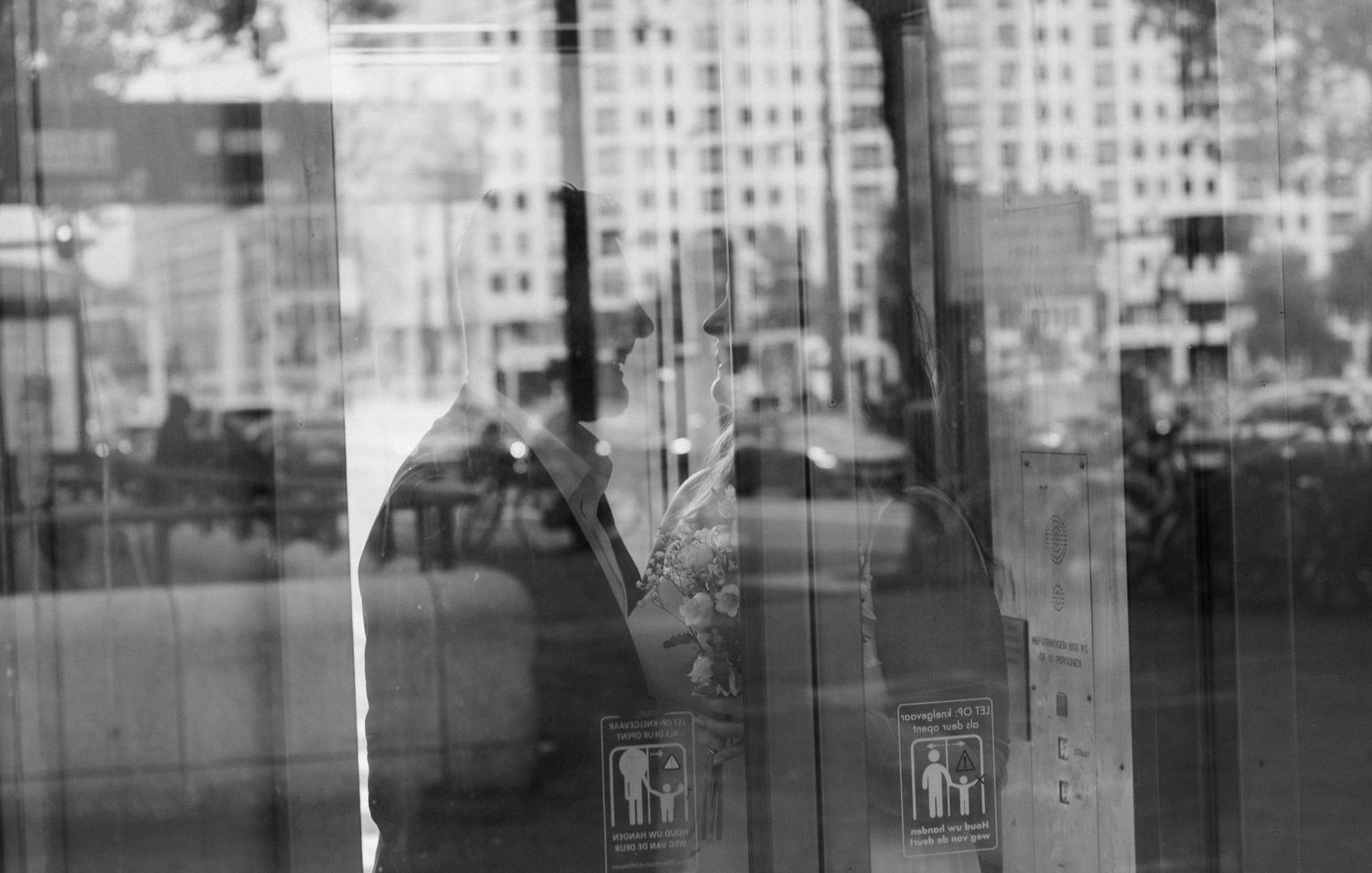 Artistic black and white reflection of a person through a glass door on a city street.