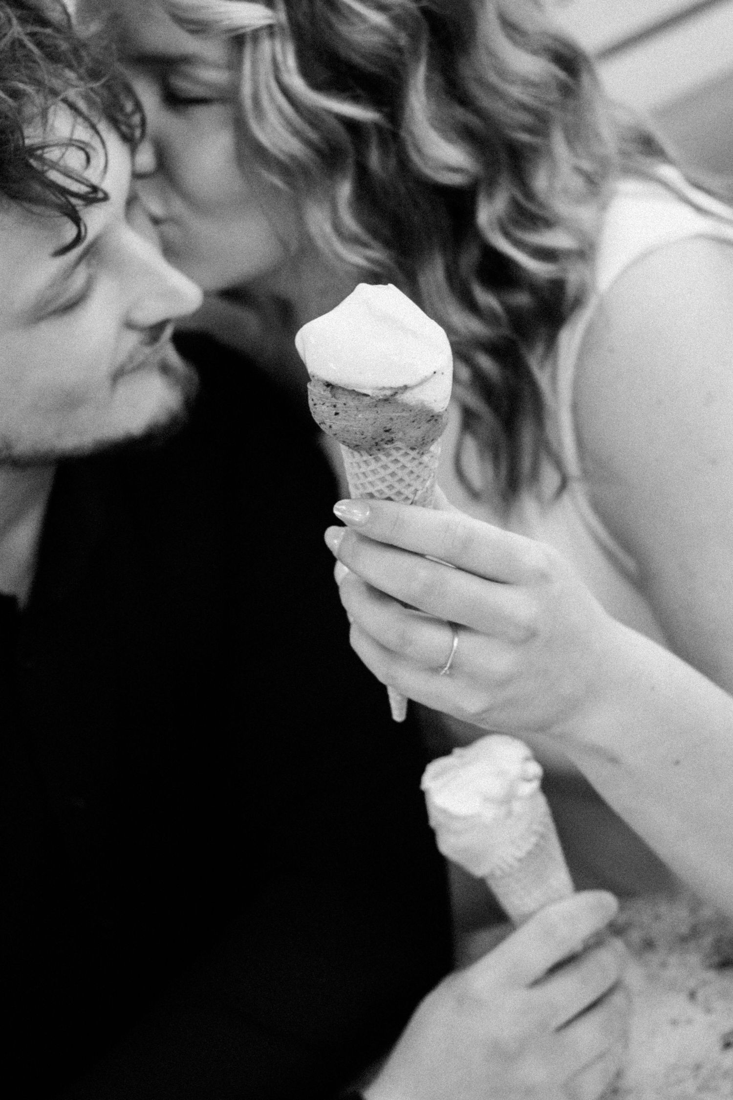 Black and white photo of a couple kissing while holding melting ice cream cones.
