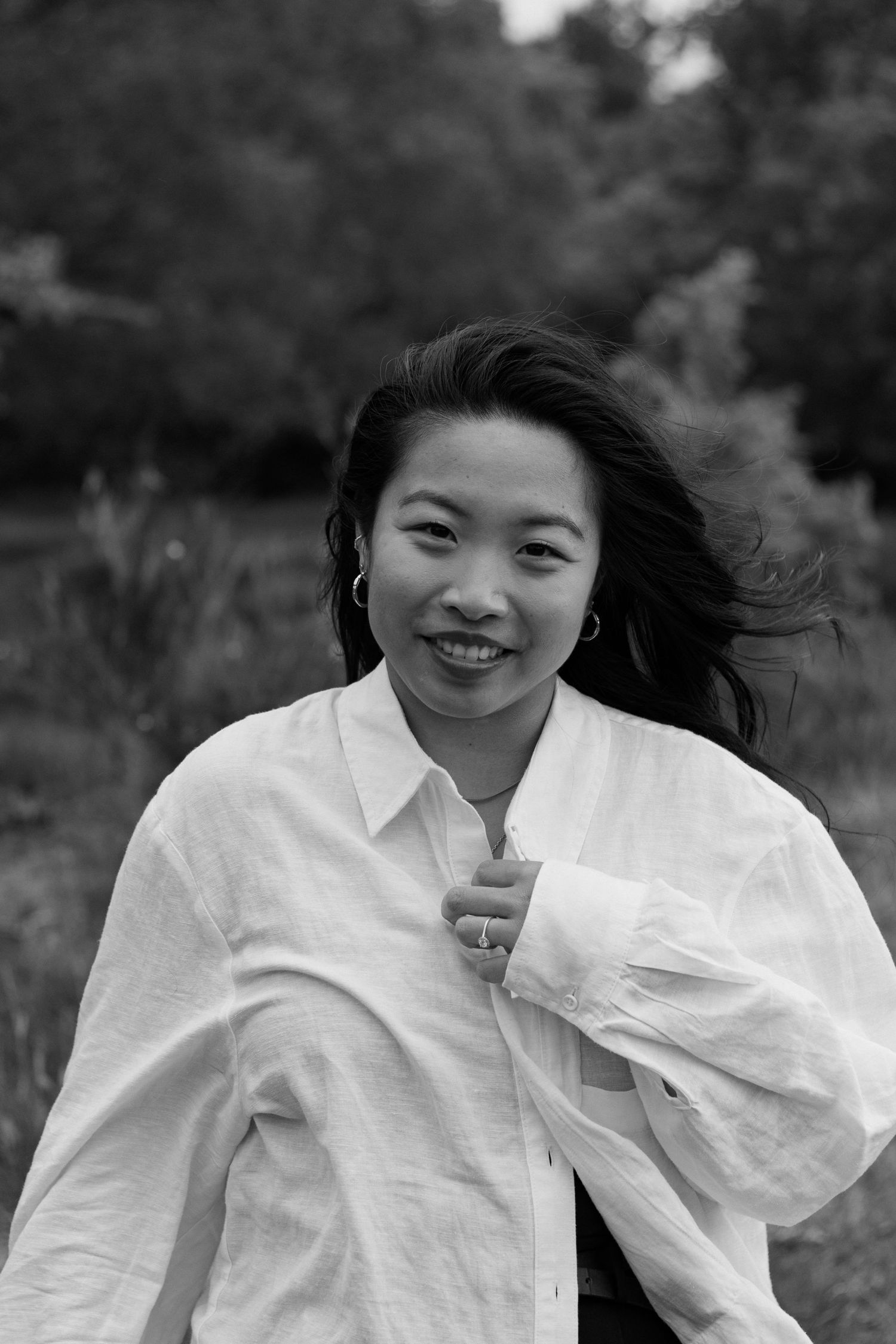 Black and white portrait of a smiling Asian woman in a white shirt outdoors in nature.