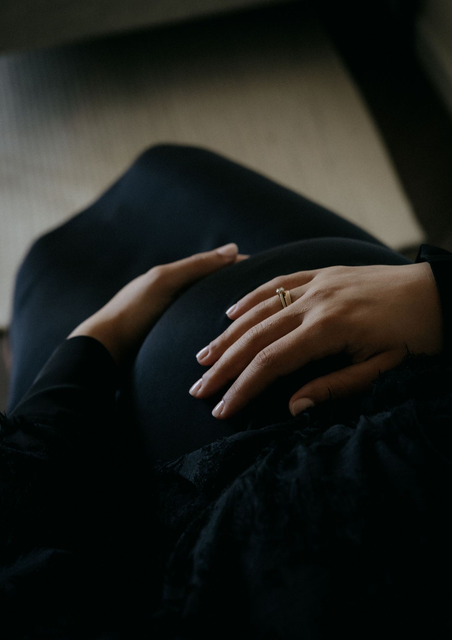 Close-up of pregnant woman's baby bump with hands resting gently, wearing a gold ring.