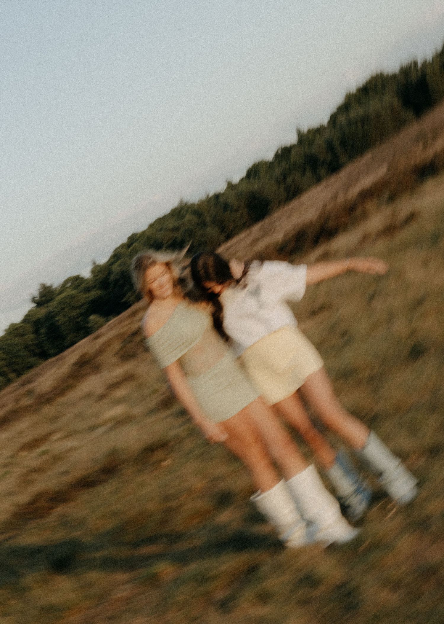 Two women embrace and laugh on a hillside in a blurred motion outdoor photo.