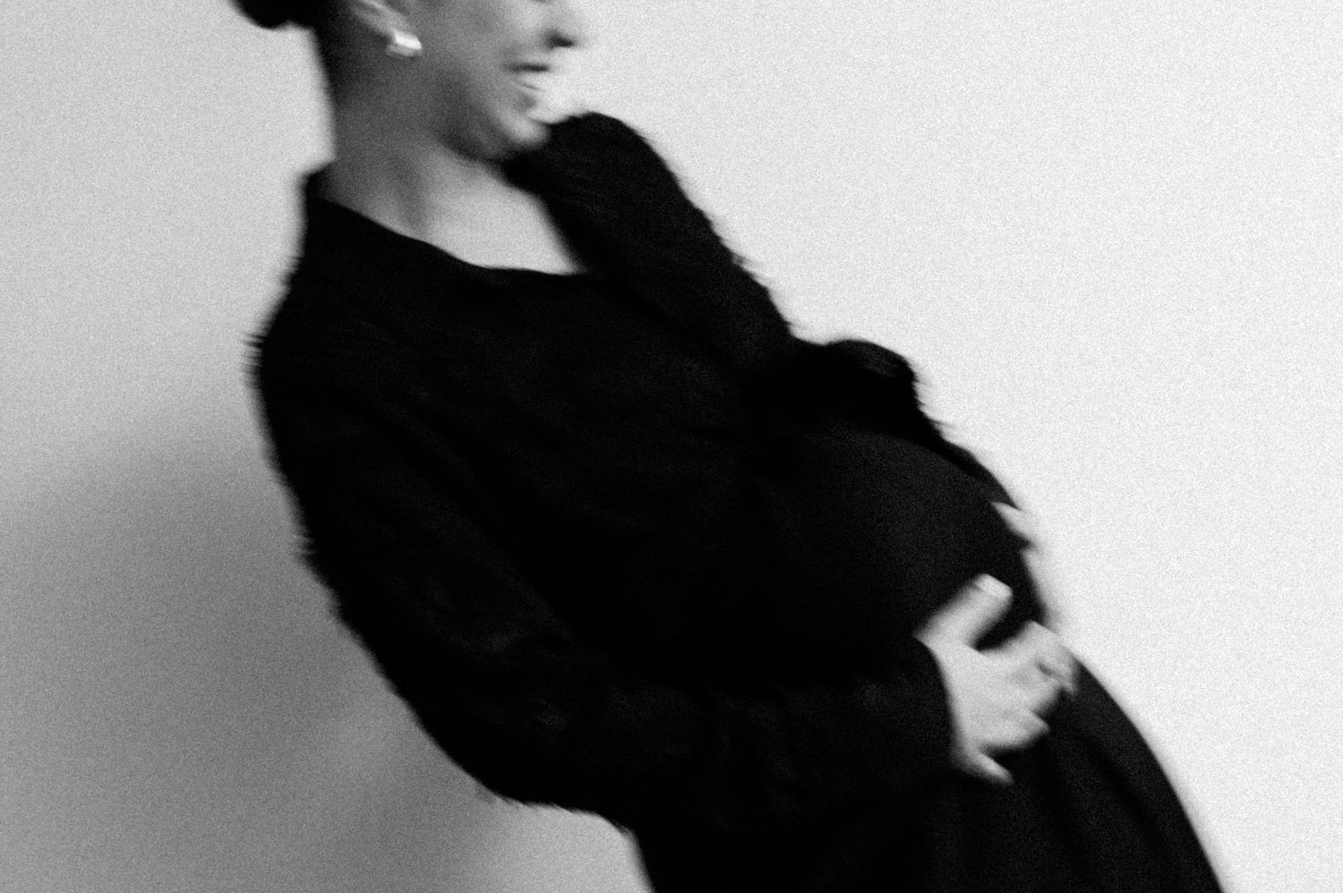 Black and white photo of a pregnant woman in an elegant black outfit posing gracefully.