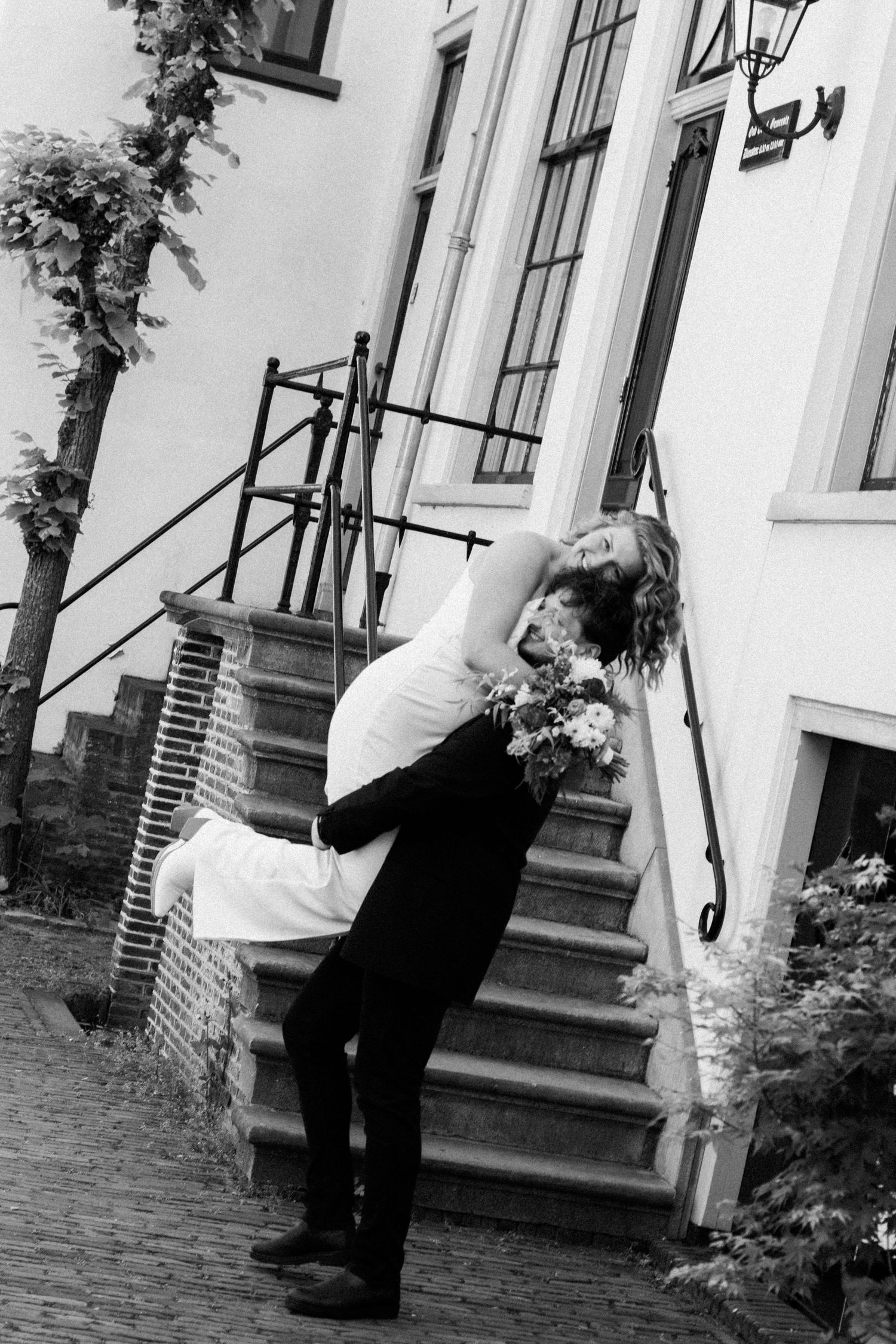 Black and white photo of groom dipping bride on outdoor steps near a historic building.