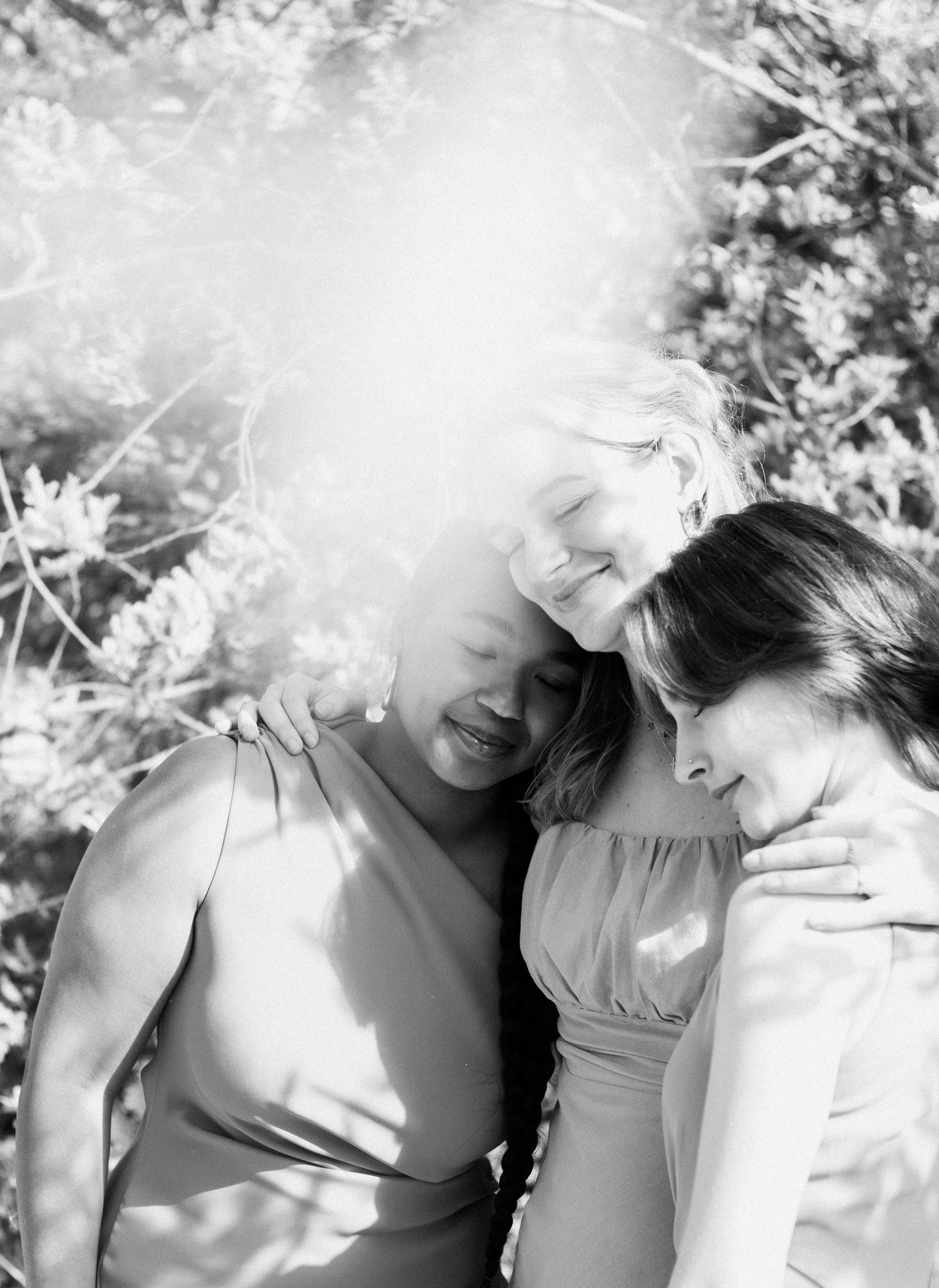 Two bridesmaids embrace joyfully in dappled sunlight in a beautiful black and white wedding photo.