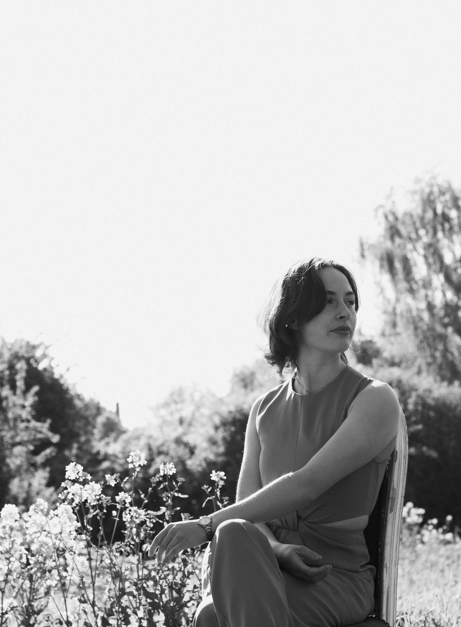 Black and white portrait of a woman sitting outdoors among flowers in a garden setting.