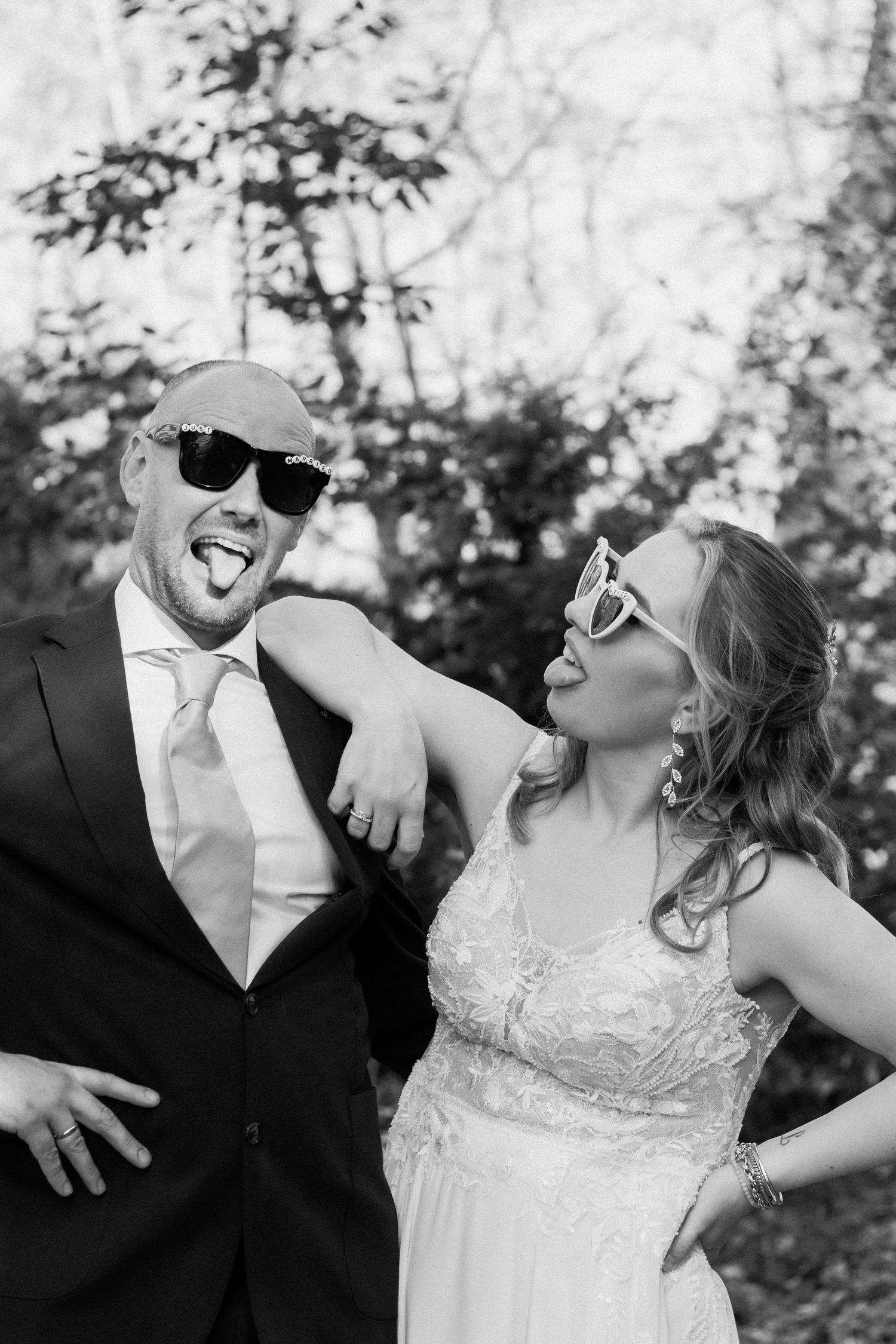Playful black and white wedding photo of couple wearing novelty sunglasses and sticking tongues out.