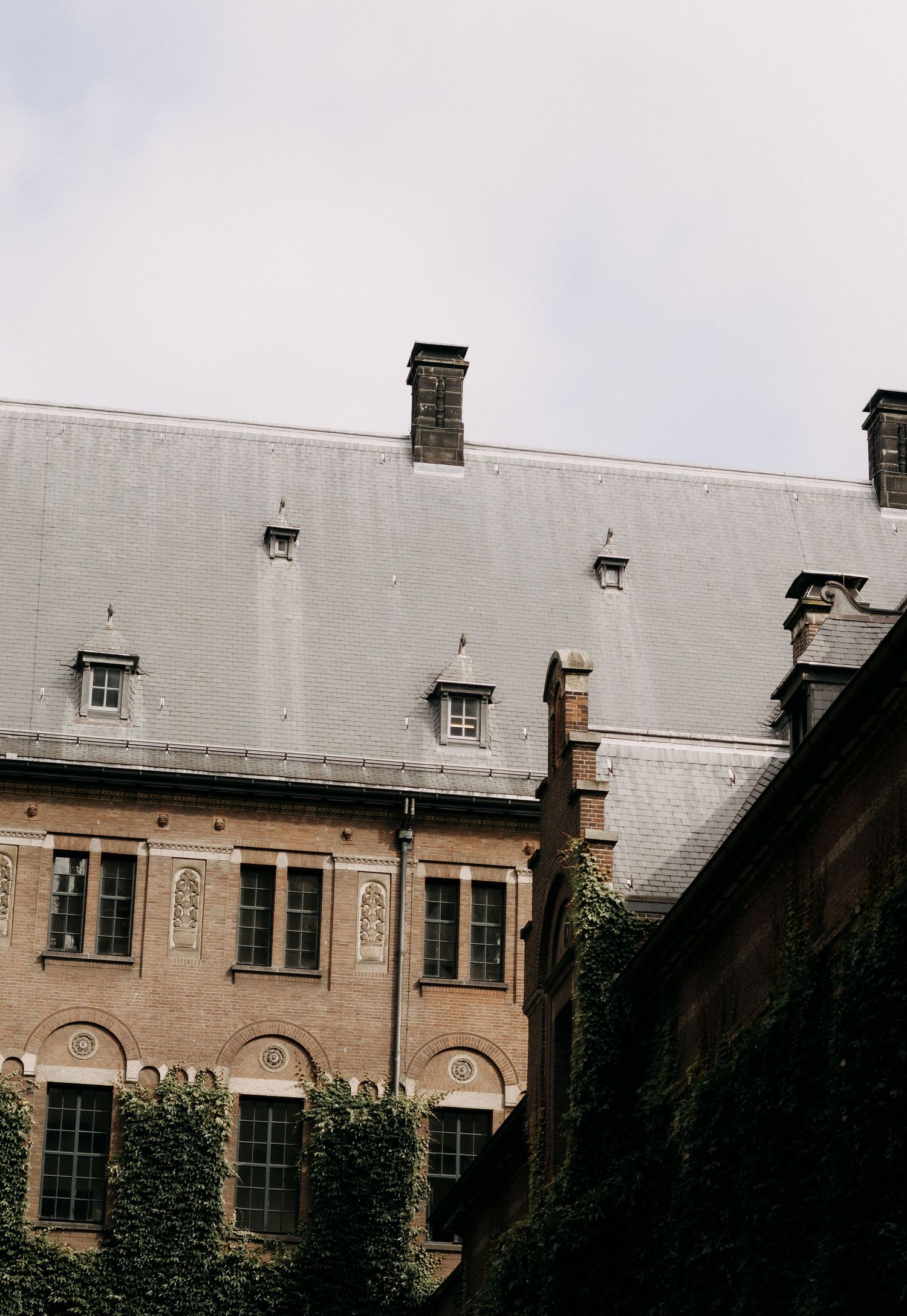 Historic stone building exterior with slate roof, chimneys, and ivy-covered walls.