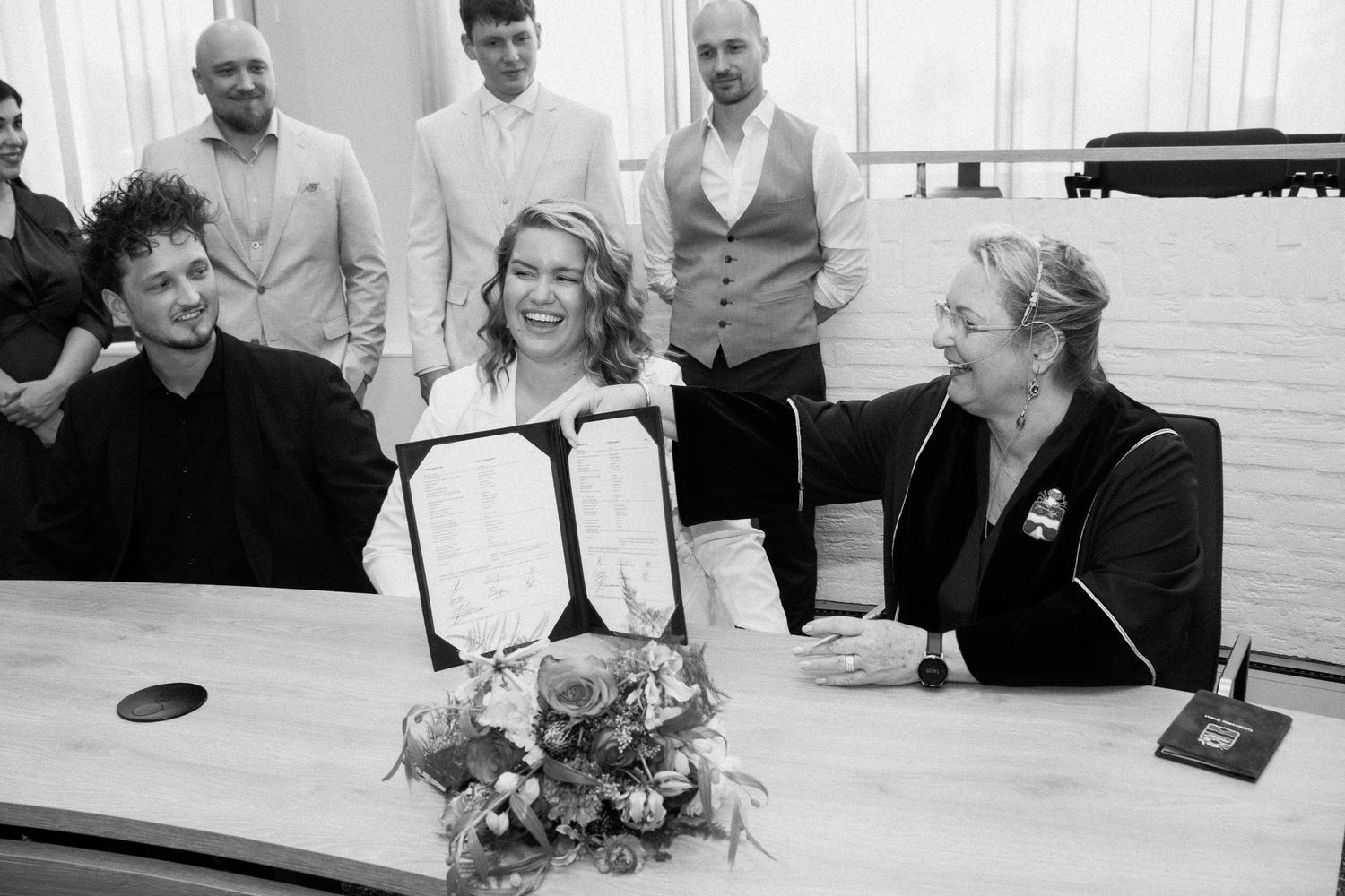 Joyful wedding signing ceremony with couple and guests in black and white photo.