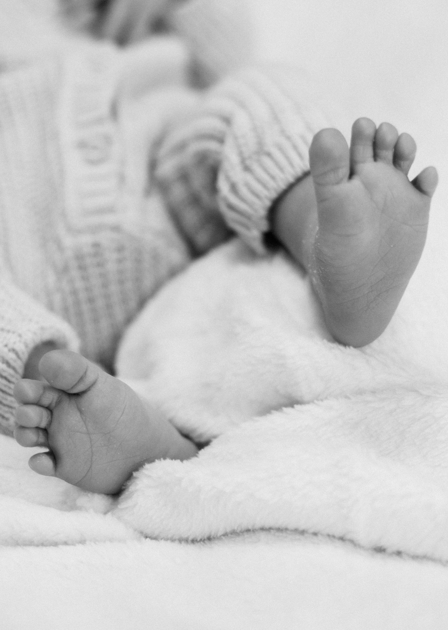 Close-up black and white photo of a newborn baby's tiny feet on a soft white blanket.