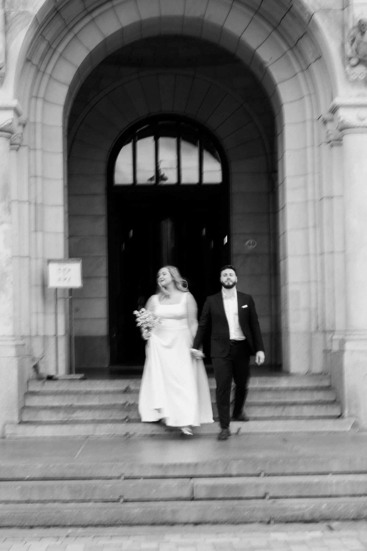 Black and white photo of newlyweds descending stone steps of a grand building after ceremony.