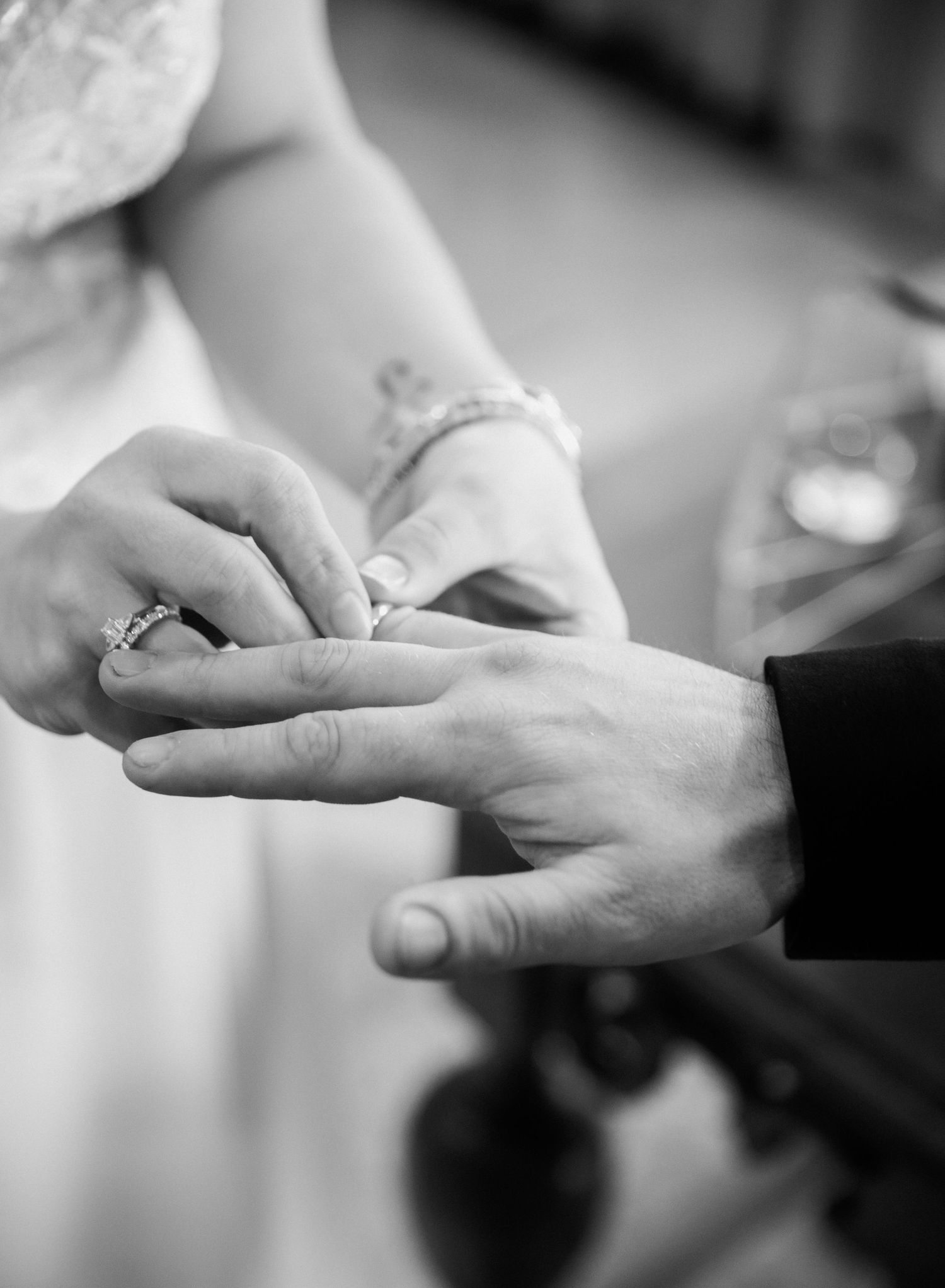 Black and white close-up of bride placing wedding ring on grooms finger during wedding ceremony.