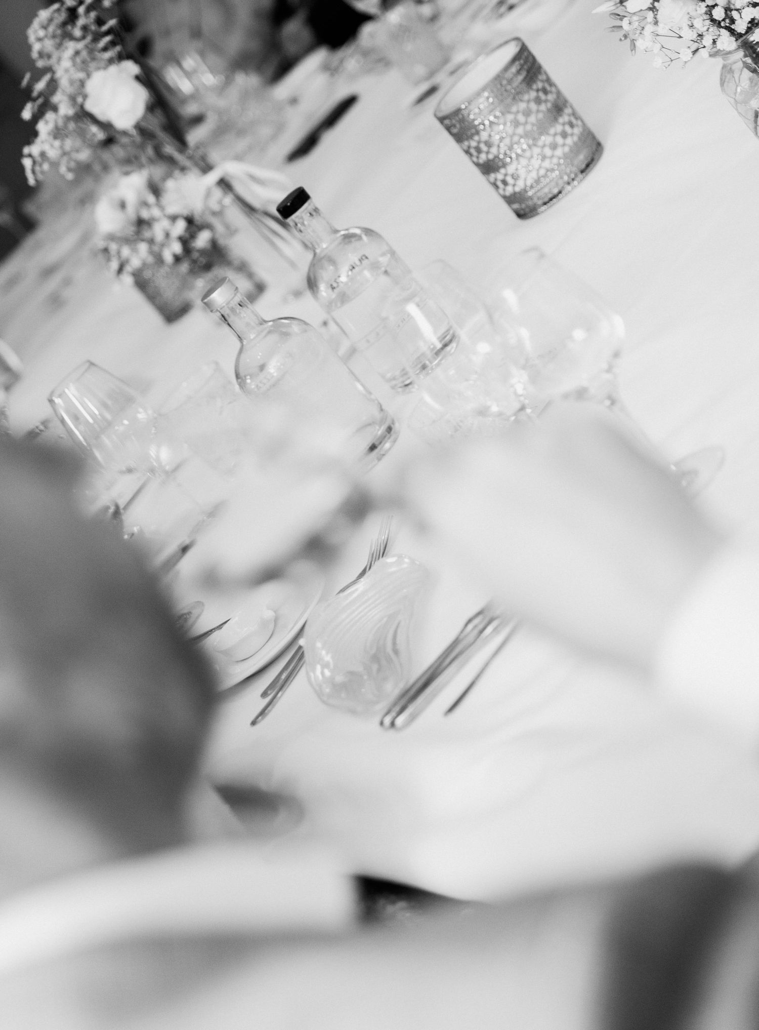 Black and white close-up of elegant wedding reception table set with glassware and candles.