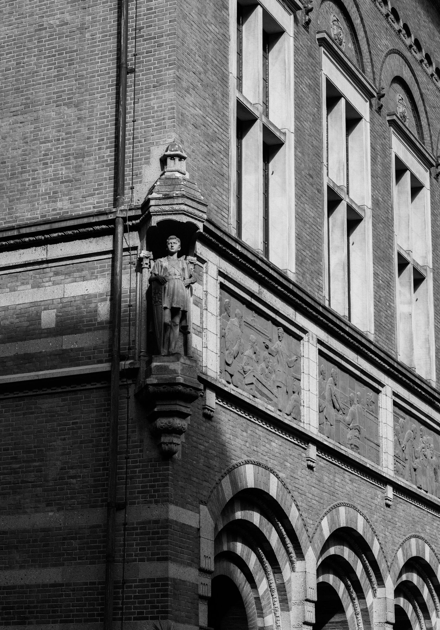 Black and white photo of ornate brick building facade with stone statue on corner.