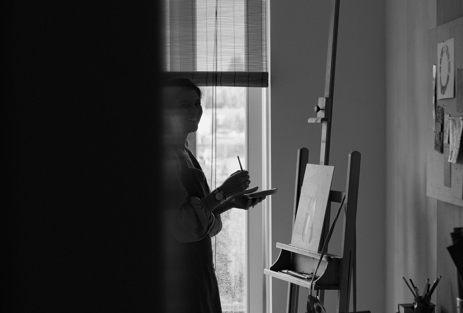 Black and white silhouette of an artist painting on an easel by a window.
