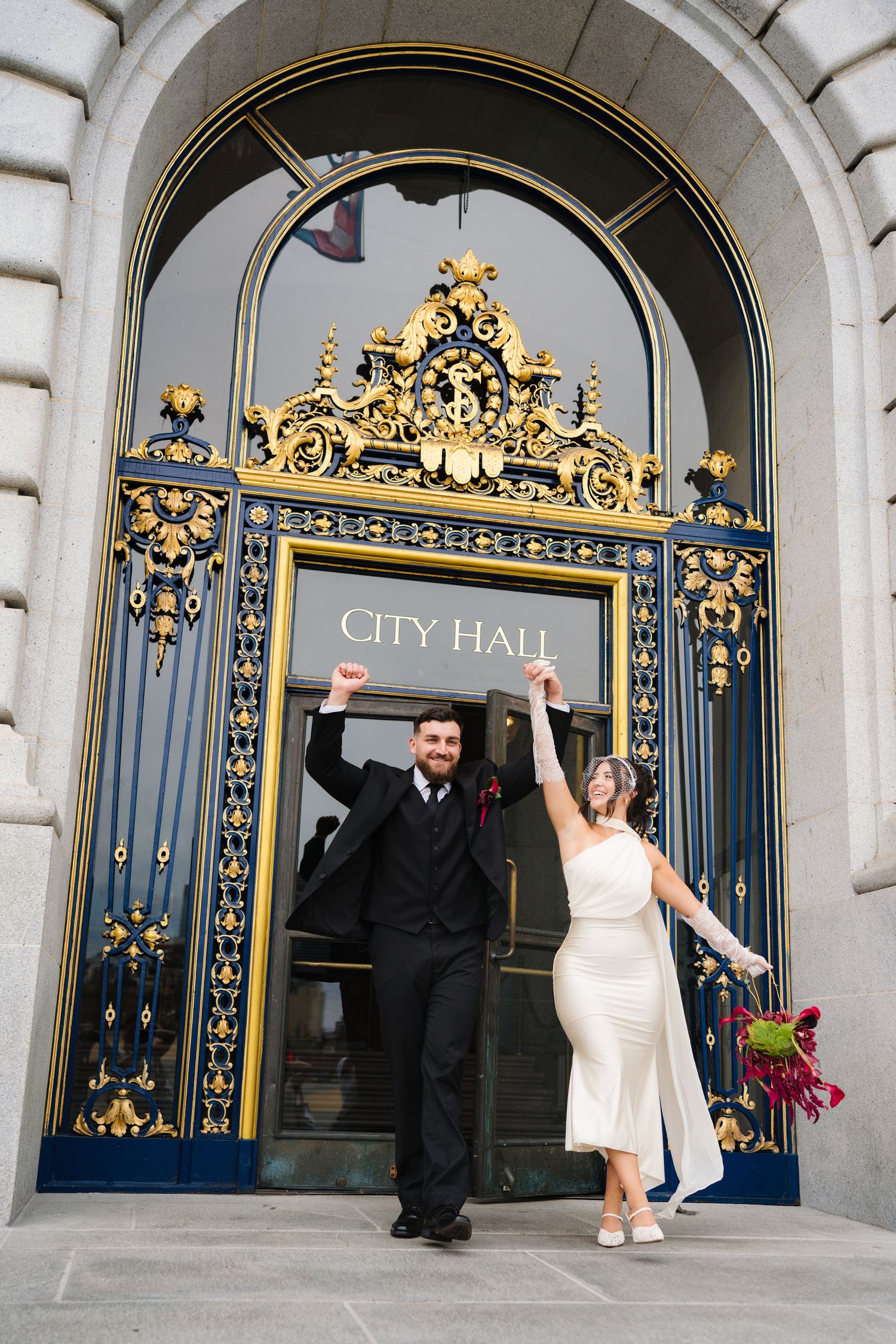Newlywed couple celebrating outside San Francisco City Hall ornate golden gates after their wedding ceremony.