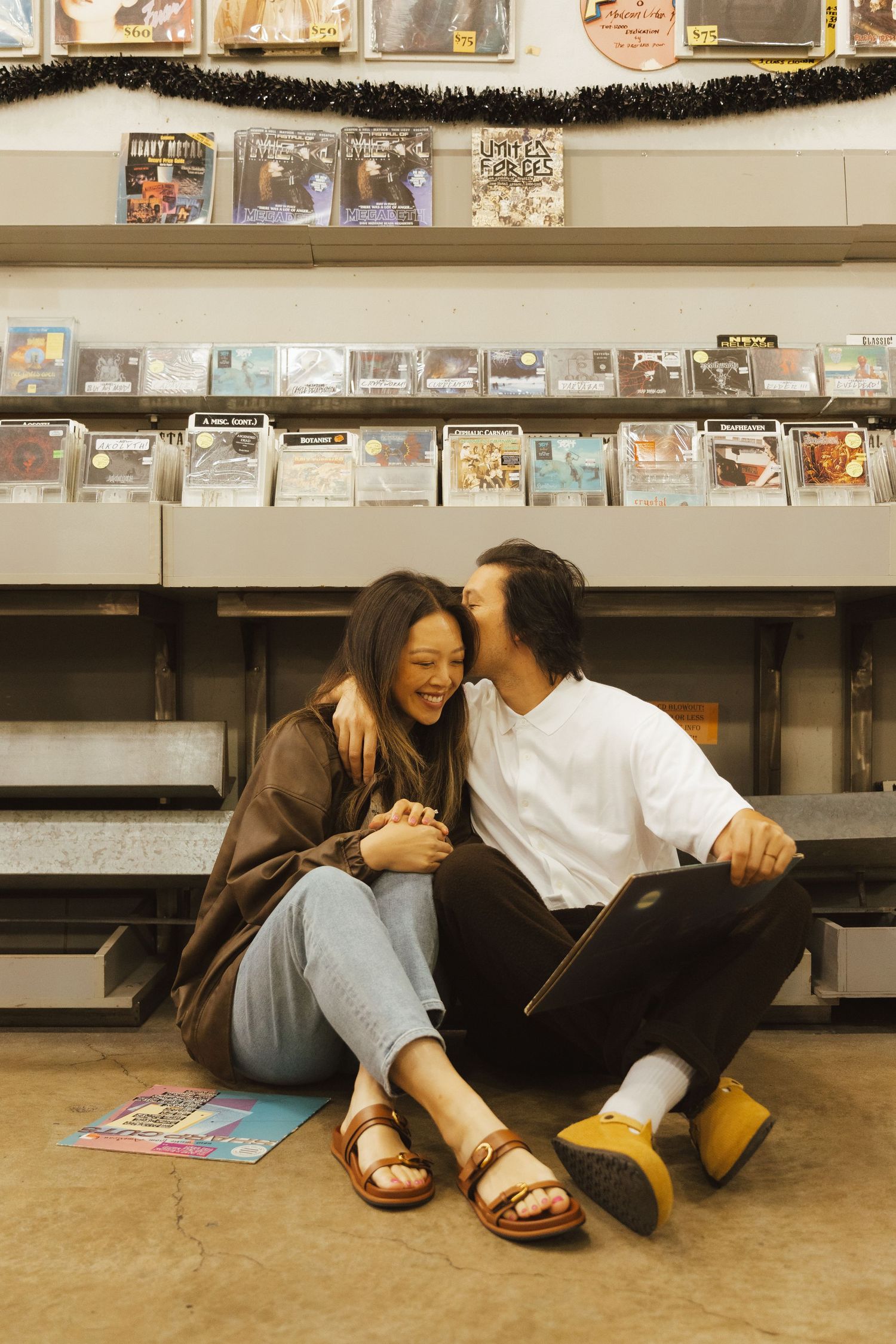 Couple sitting on floor of record store, laughing and sharing a tender moment among shelves of CDs.