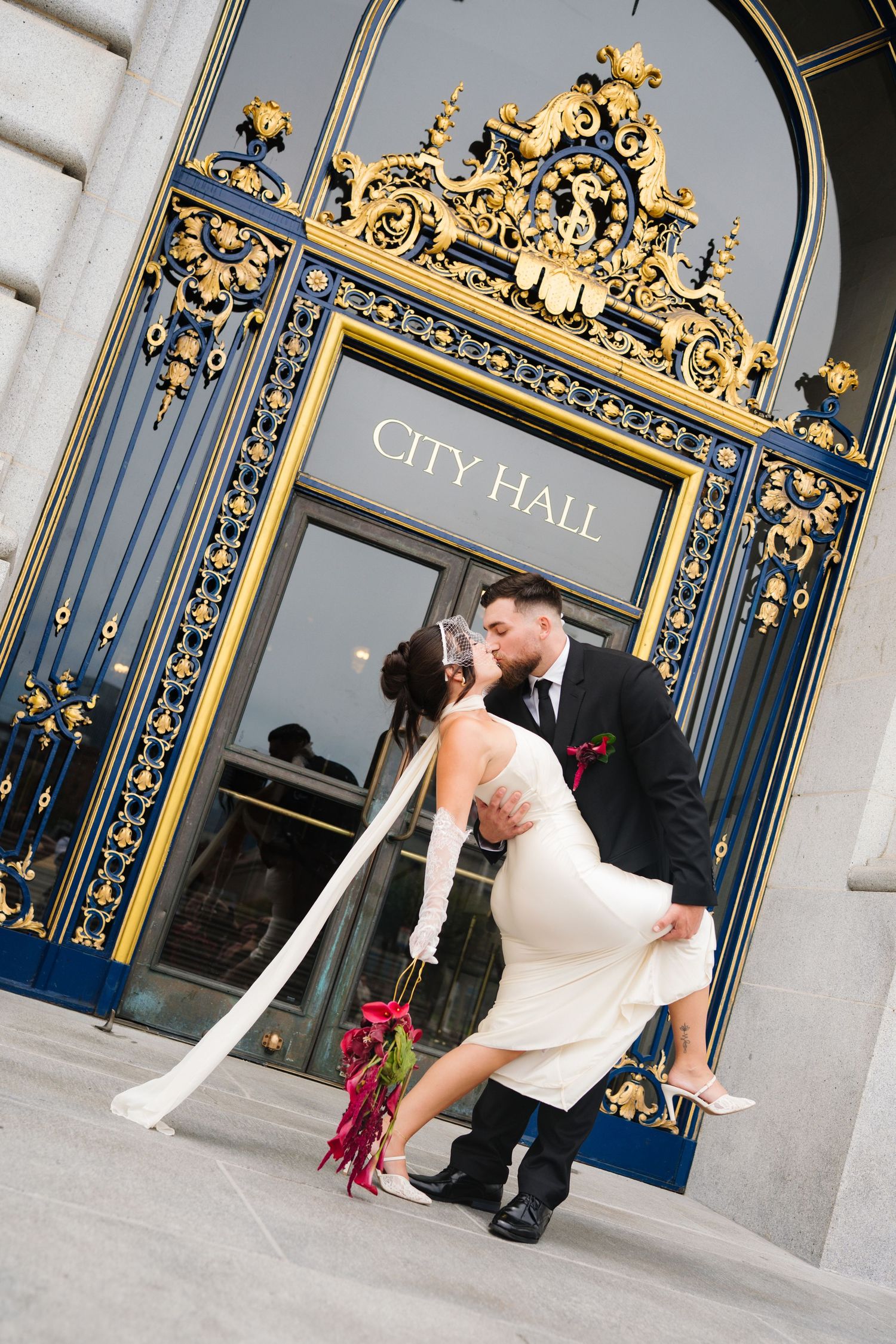 Newlyweds share a romantic dip kiss in front of San Francisco City Hall's ornate gold and blue doors.
