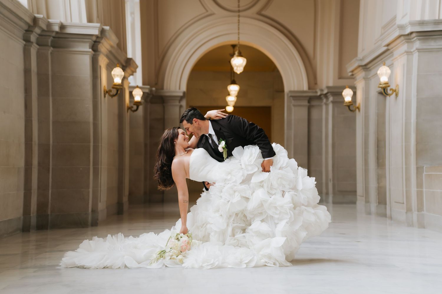 Bride in voluminous white gown shares romantic dip kiss with groom in black tux at San Francisco City Hall.