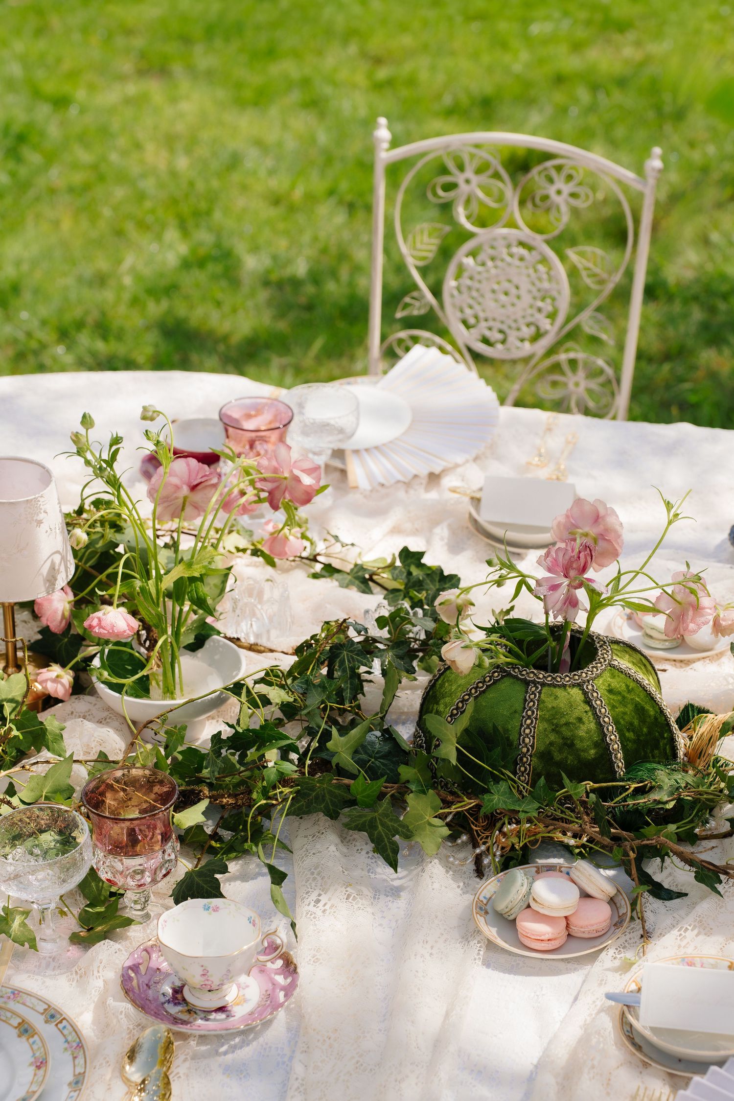 Elegant outdoor garden table setting with pink flowers, macarons, and vintage china.