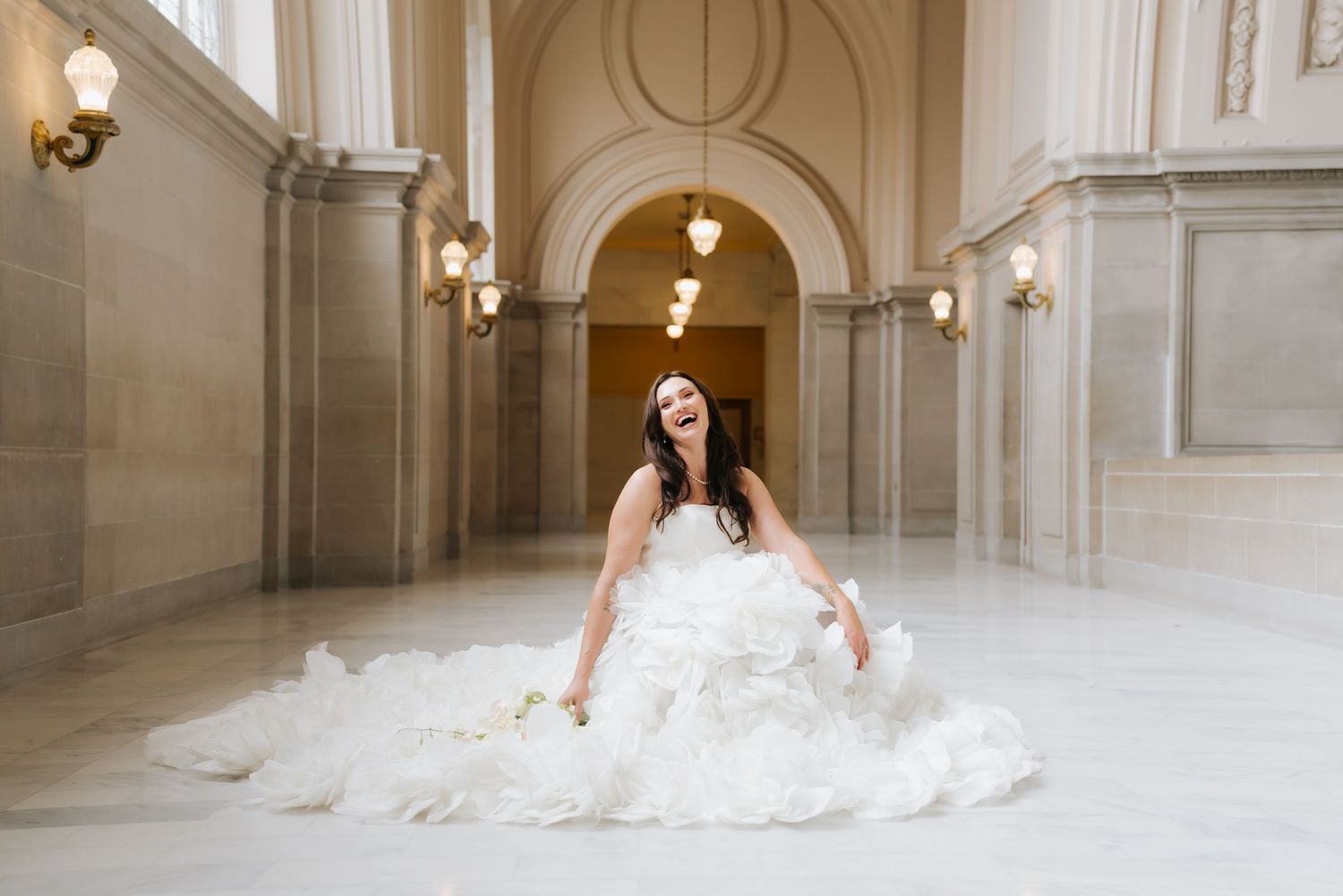 Bride in a voluminous white wedding gown laughing joyfully in an elegant marble hall.
