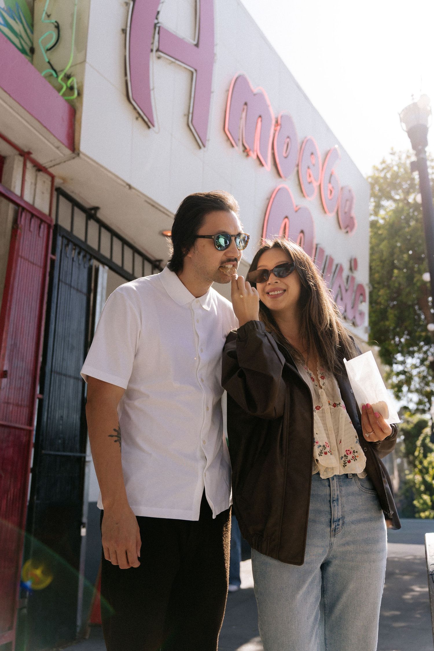 Stylish couple in sunglasses smiling outside Amoeba Music store on a sunny day.