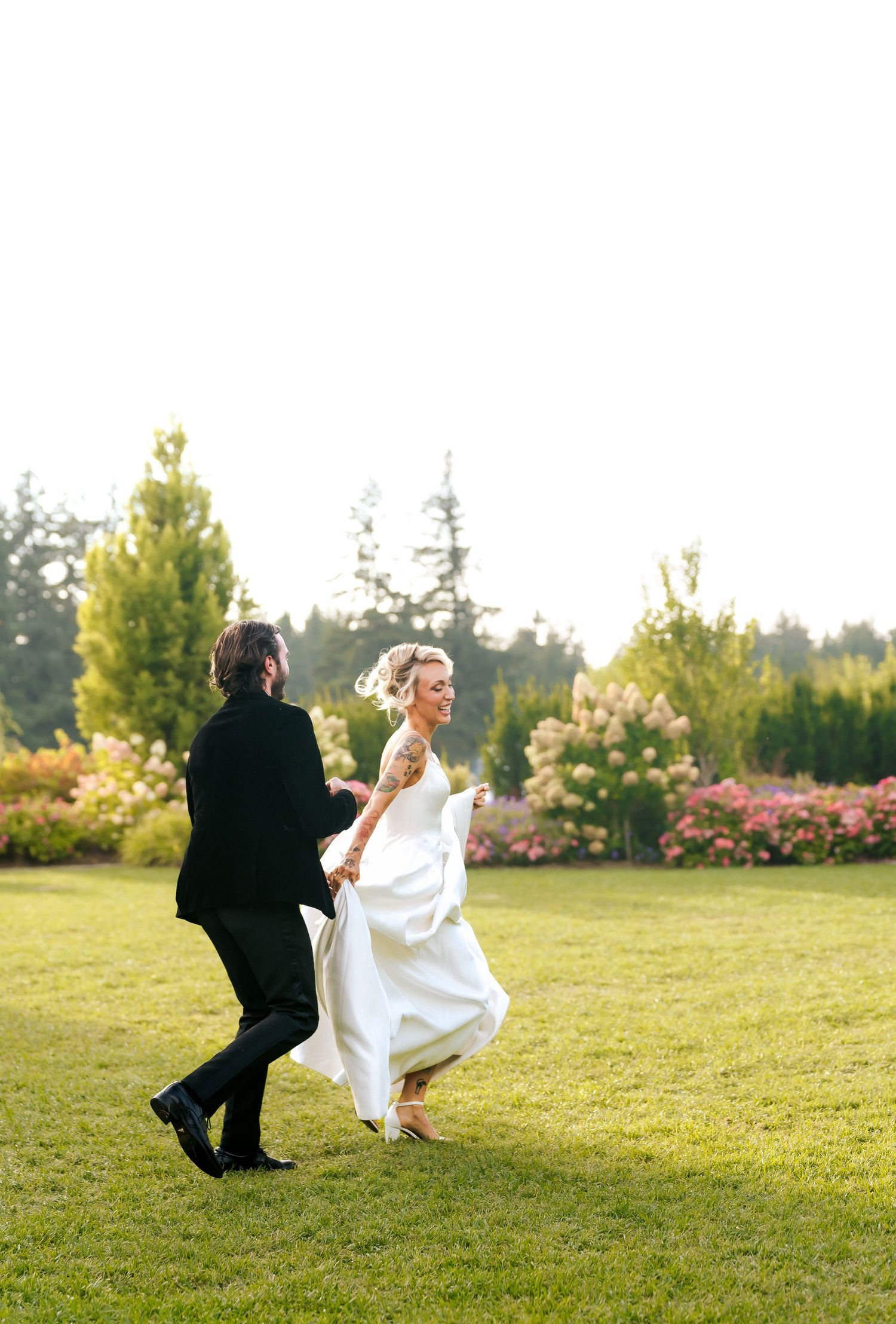 Bride and groom dancing joyfully on green lawn surrounded by colorful garden blooms at outdoor wedding.