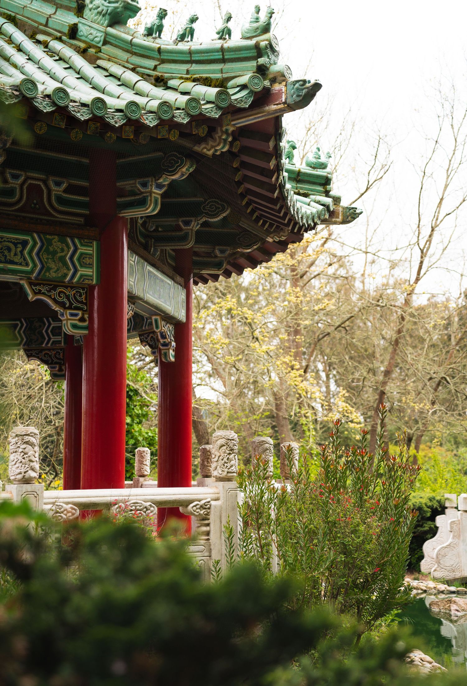 Traditional Chinese pavilion with red columns and ornate green tiled roof in a garden.