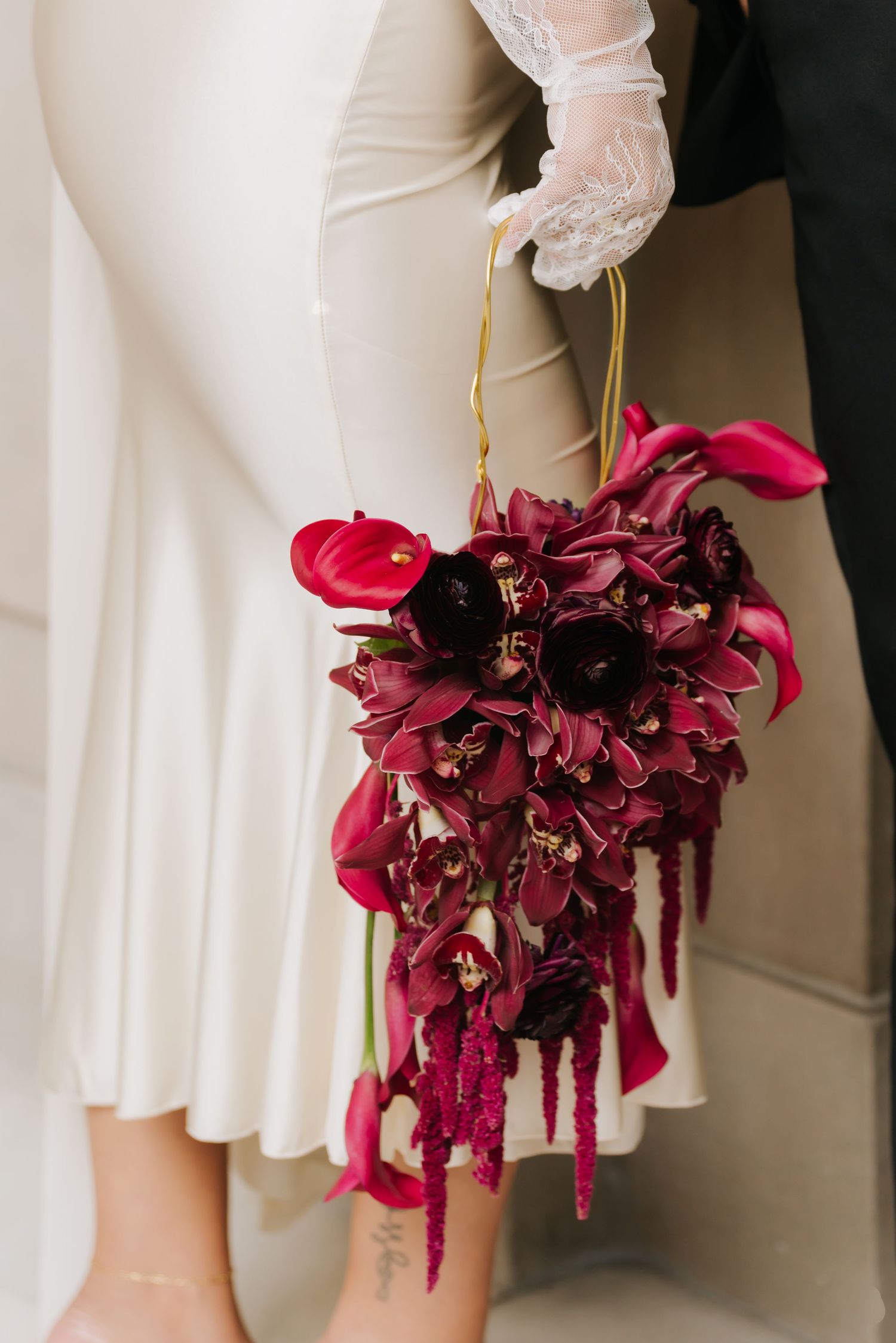Bride holding a cascading deep burgundy wedding bouquet with orchids, tulips, and amaranthus, wearing a white gown and lace gloves.