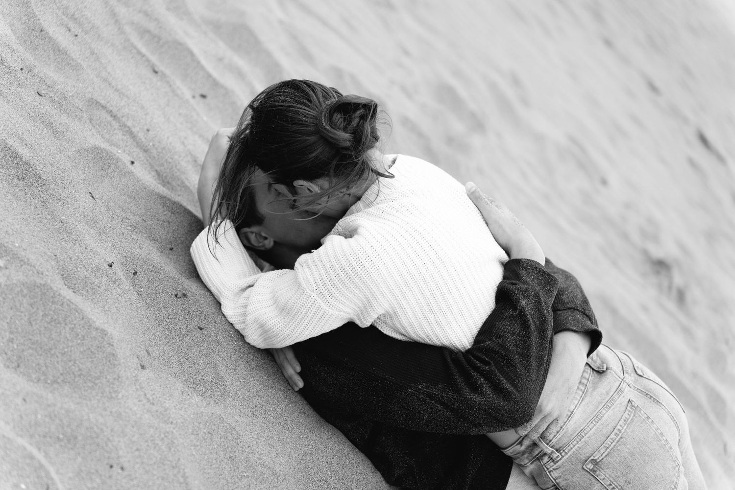 Black and white photo of two people embracing on a sandy beach, sharing an intimate moment.