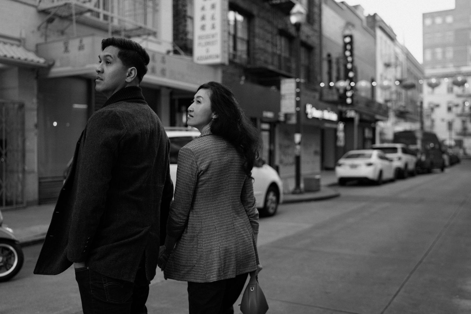 Black and white photo of a couple walking hand in hand down a city street.