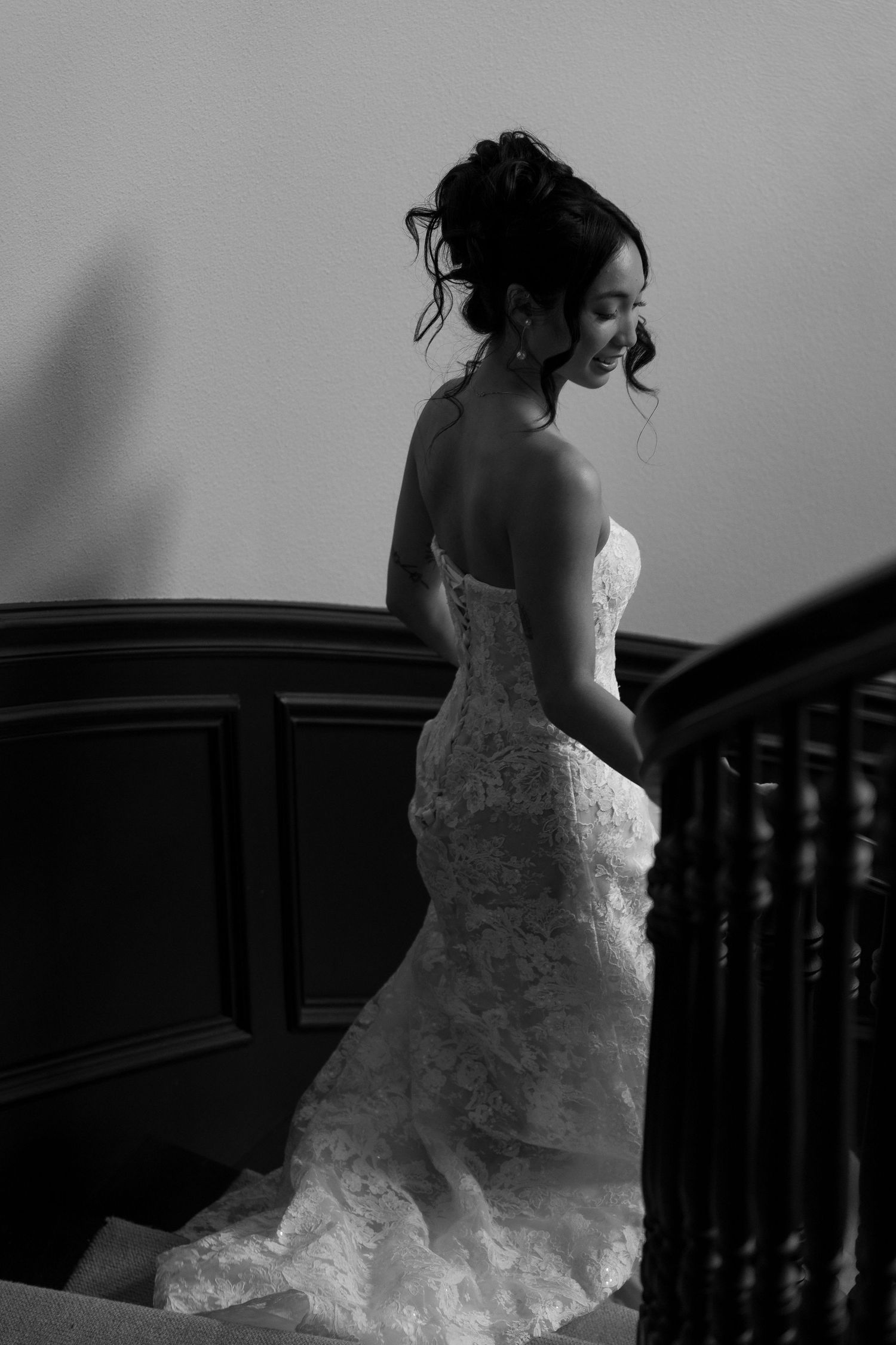 Black and white photo of bride in strapless lace mermaid gown on elegant staircase.
