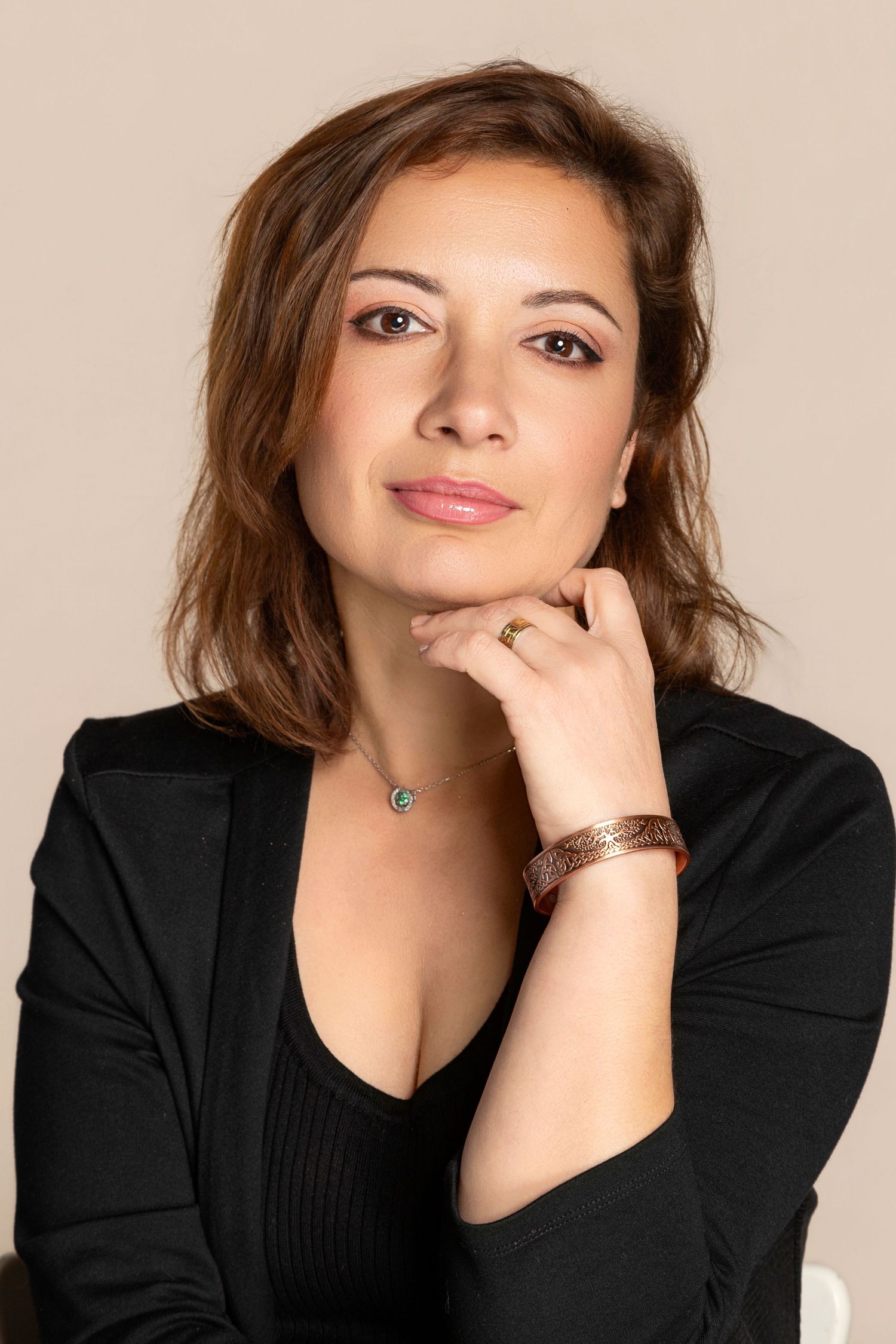 Professional woman in black blazer posing thoughtfully with hand near chin, wearing bracelet and necklace.