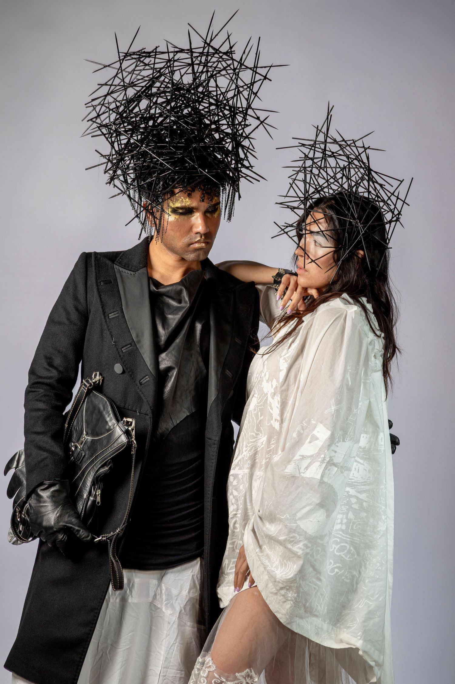 Two models in avant-garde black spiked headpieces, one in black suit, one in white dress, posing dramatically in studio.