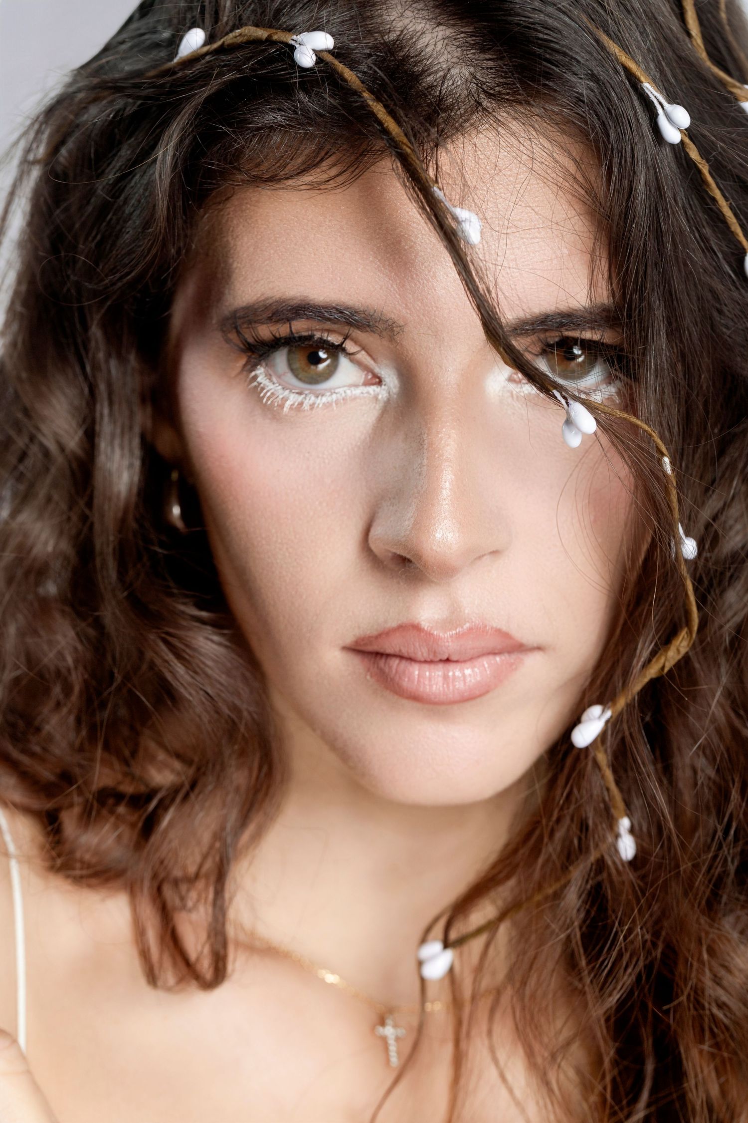 Close-up portrait of a brunette woman with white floral hair accessories and artistic eye makeup.
