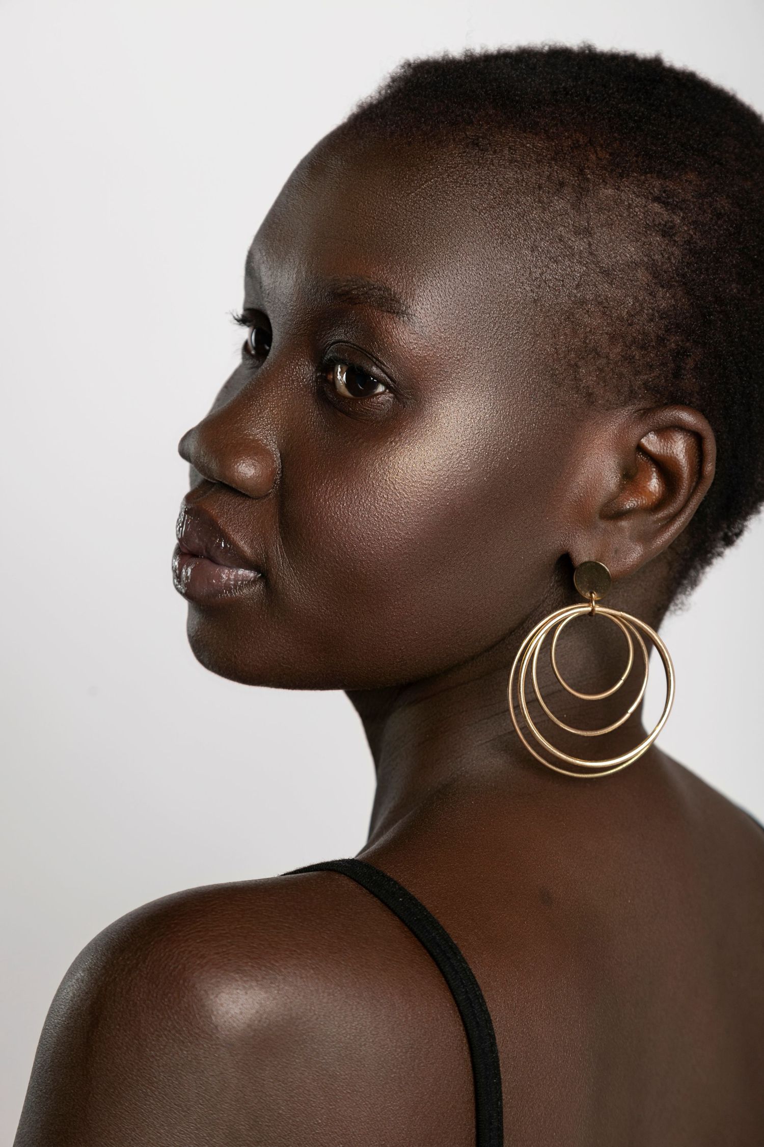 Profile portrait of a young Black woman with short hair wearing large gold hoop earrings.
